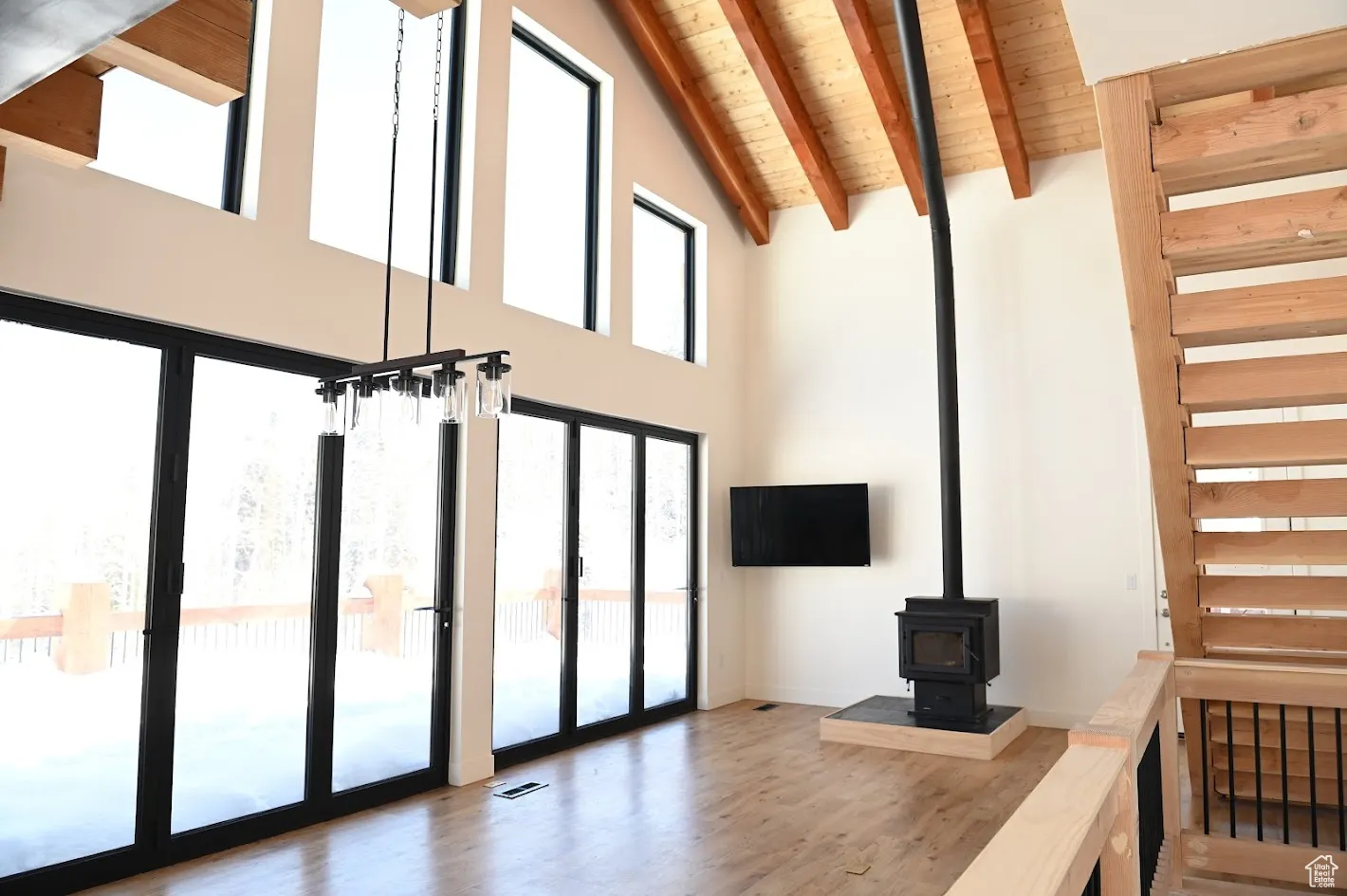 Unfurnished living room featuring high vaulted ceiling, wooden ceiling with exposed beams, wood finished floors, a wood stove, and stairway