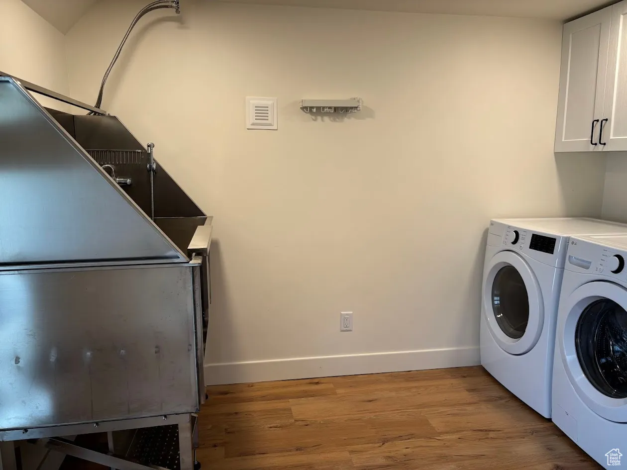 Washroom featuring cabinet space, washer and dryer, light wood-style floors, and baseboards