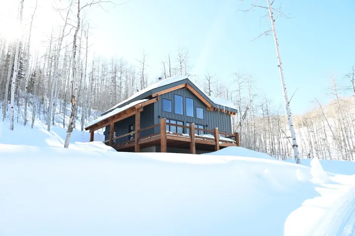 Snow covered back of property featuring board and batten siding and a wooden deck