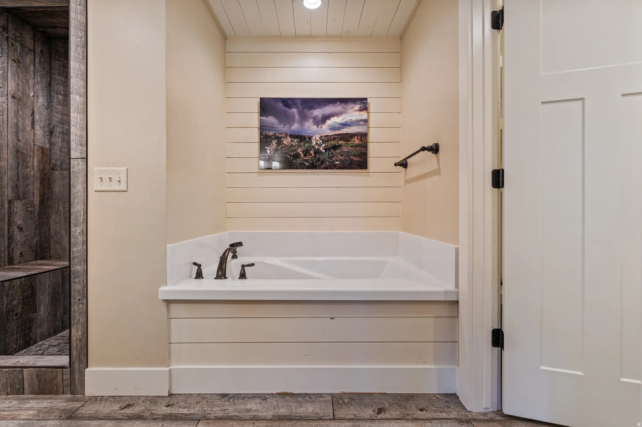 Built-in bathtub with dark bronze fixtures, shiplap wall accents, wood-finish flooring, and a barn wood-style shower enclosure