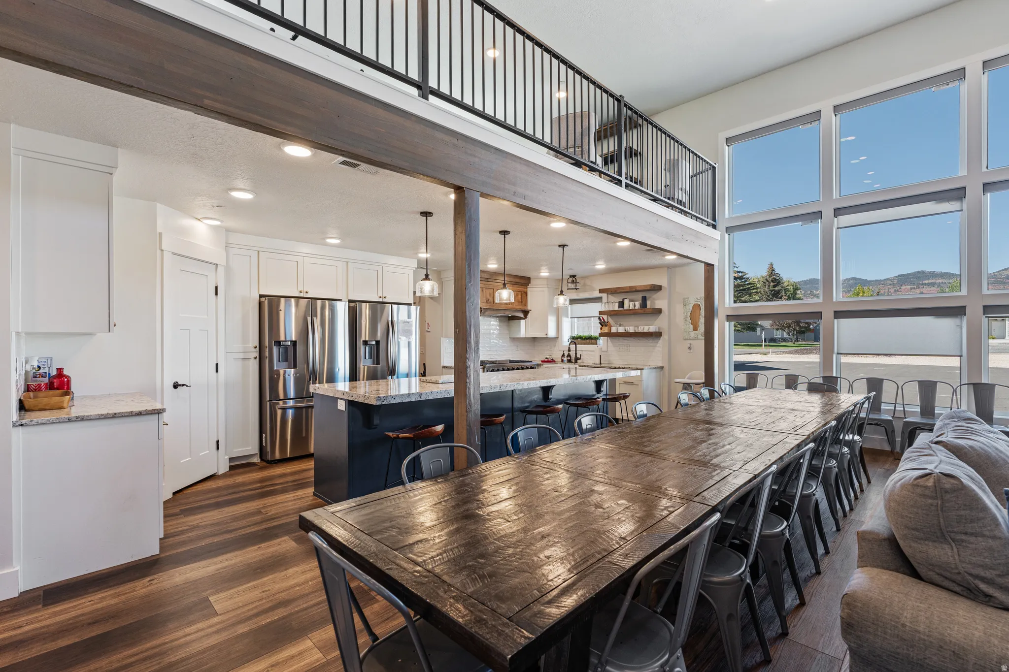 Soaring ceilings, expansive window wall, wood-finish flooring, open-concept kitchen, and an upper-level balcony