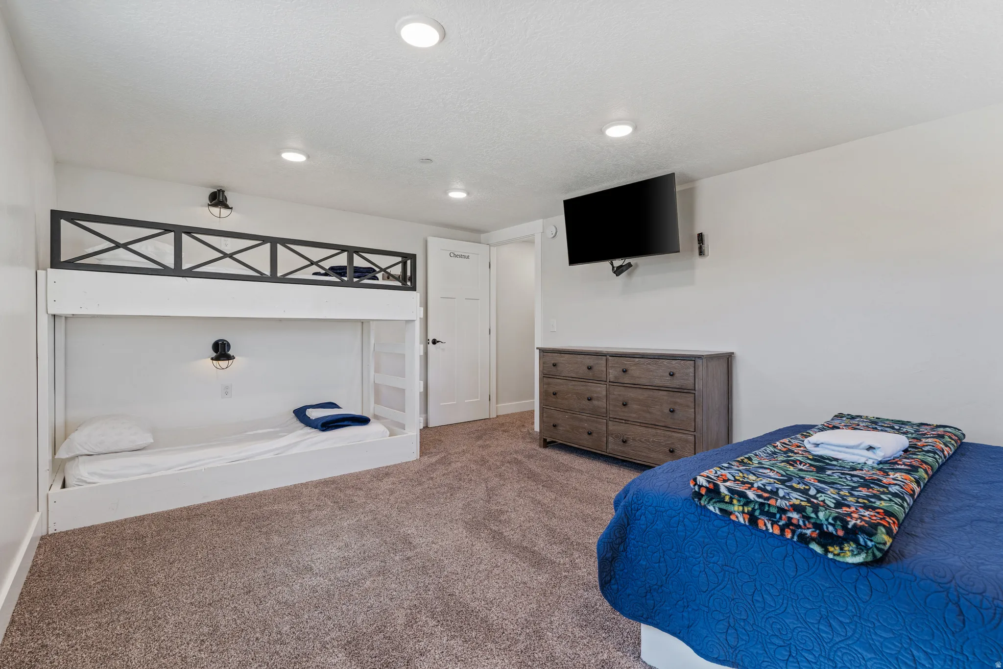 Built-in bunk bed with decorative railing and integrated wall sconces, complemented by recessed ceiling lighting and carpeting