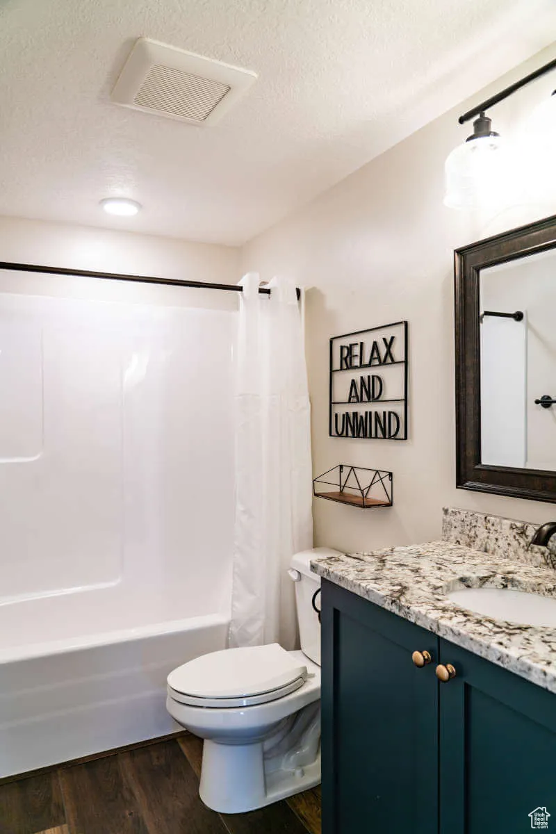 Bathroom with vanity, toilet, shower / tub combo with curtain, wood finished floors, and a textured ceiling