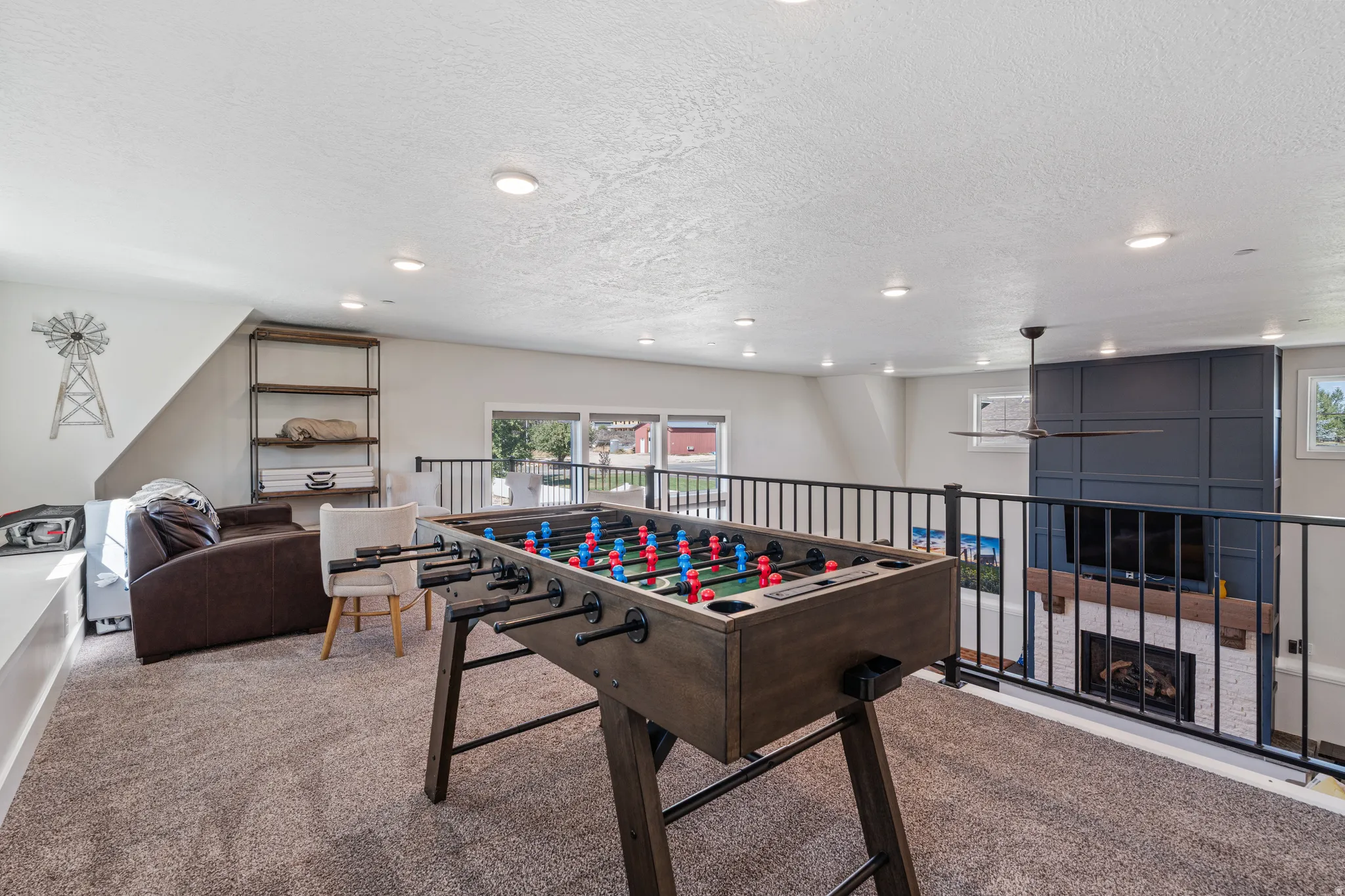 Carpeted loft area with recessed lighting, black metal railing overlooking the lower level, and a ceiling fan
