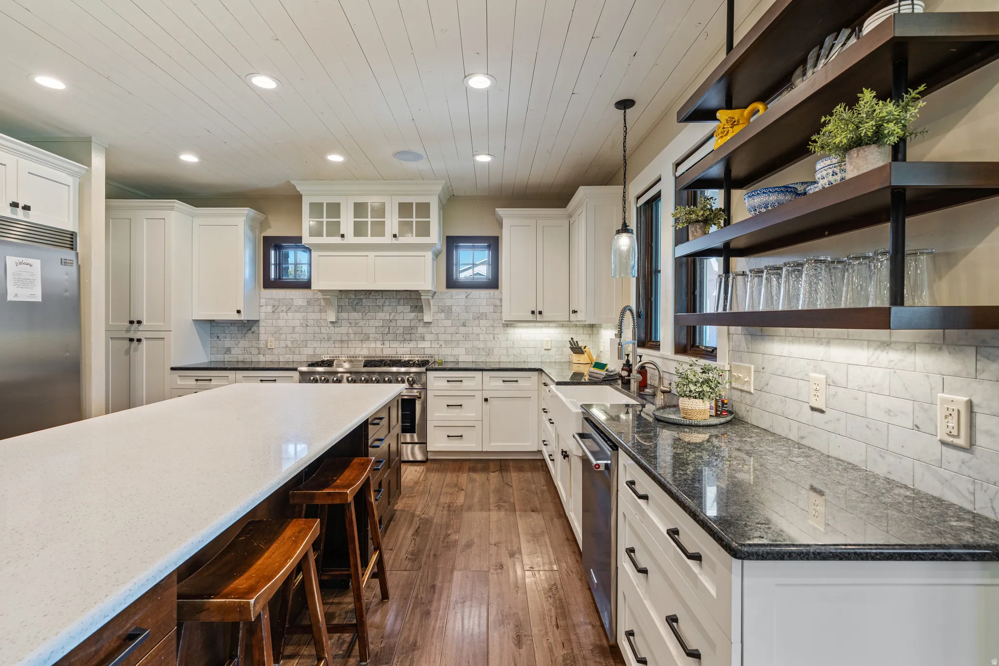 Expansive kitchen island with a light-toned countertop, white cabinetry with dark hardware, wood-finish flooring, a white subway tile backsplash, and dark countertops