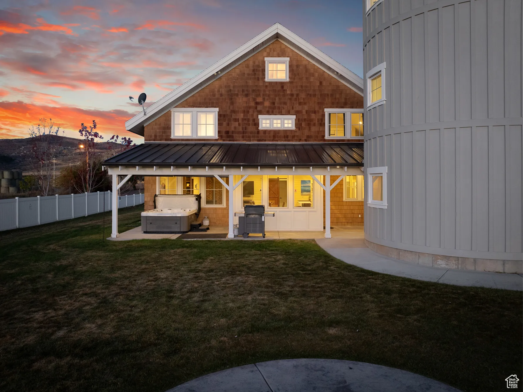 Back of property at dusk with a hot tub, a patio, a standing seam roof, and metal roof