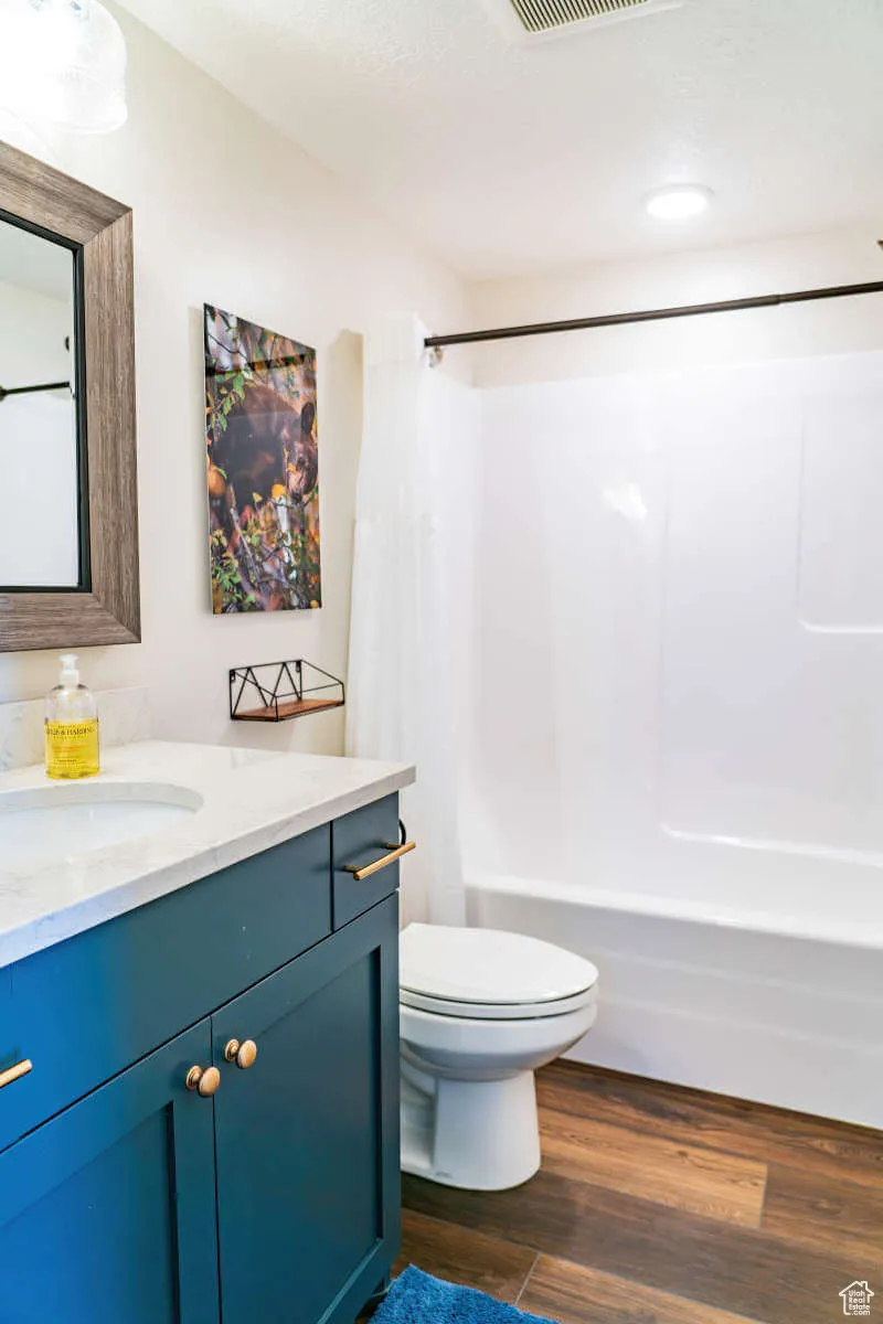 Bathroom featuring vanity, shower / bath combo with shower curtain, toilet, and wood finished floors