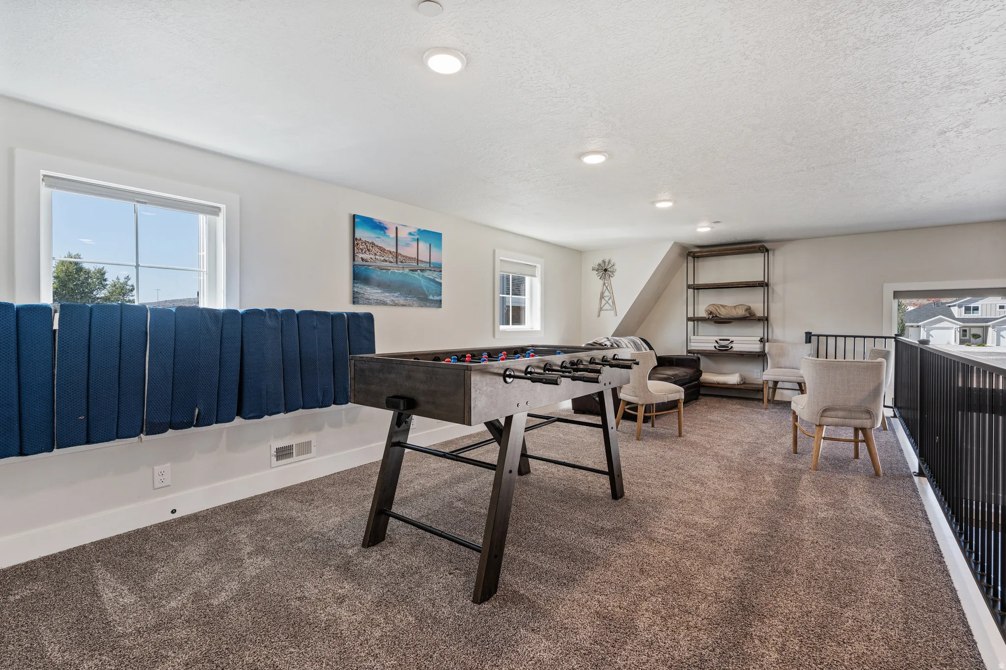 Carpeted upper-level space featuring recessed lighting, multiple windows, a sloped ceiling, and an open metal railing