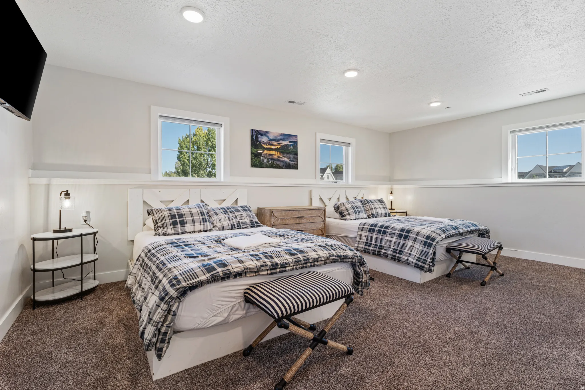 Bright secondary bedroom suite featuring multiple windows with natural light, neutral wall finishes with wainscoting detail, carpeted flooring, and ample space accommodating multiple bed configurations