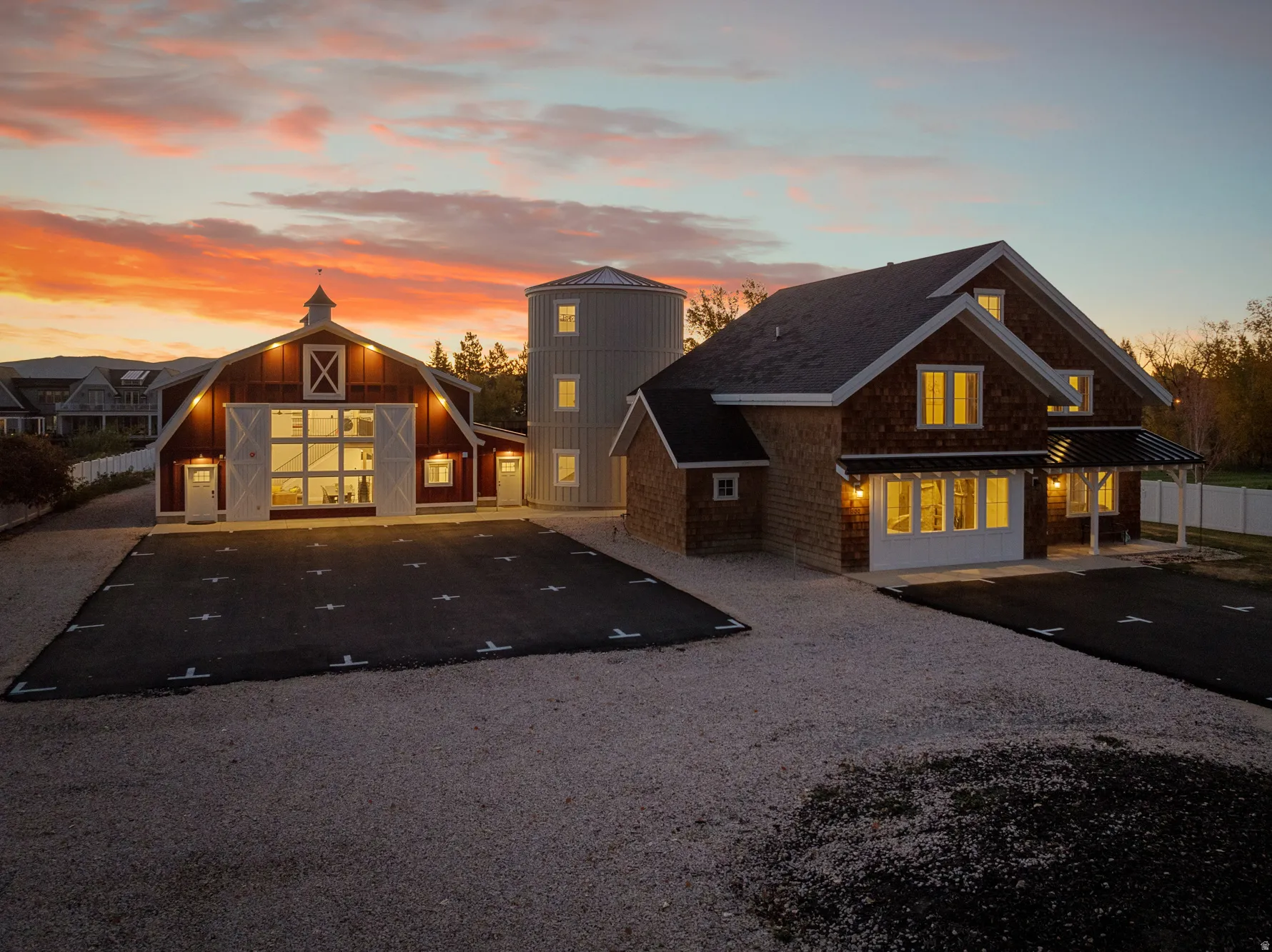 Multiple structures with shingle siding and dark roofs, including a barn-style building with large glass doors and a silo-style structure with multiple windows