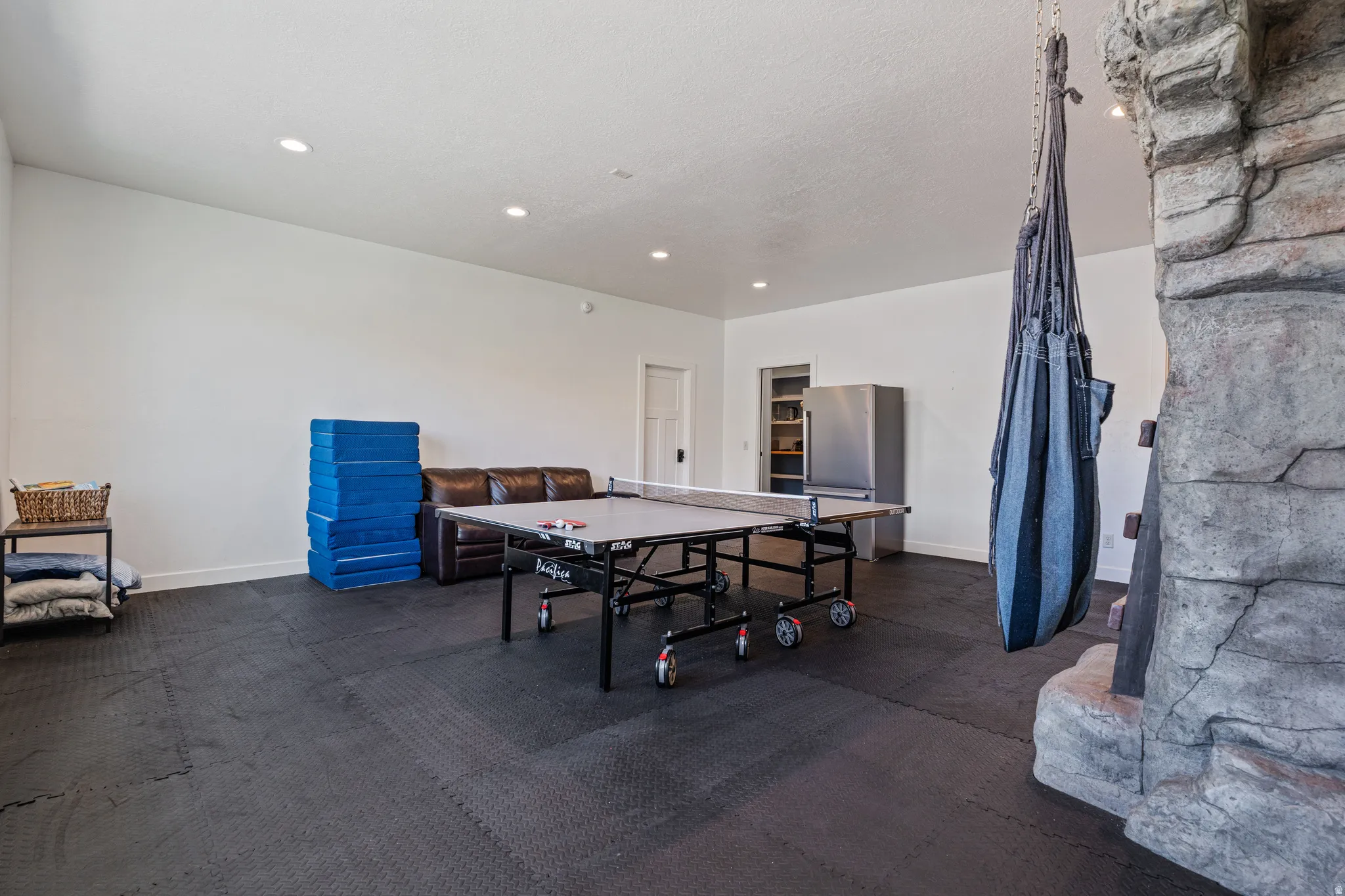 Spacious recreation room featuring recessed lighting, durable floor tiling, and a stone-clad architectural element