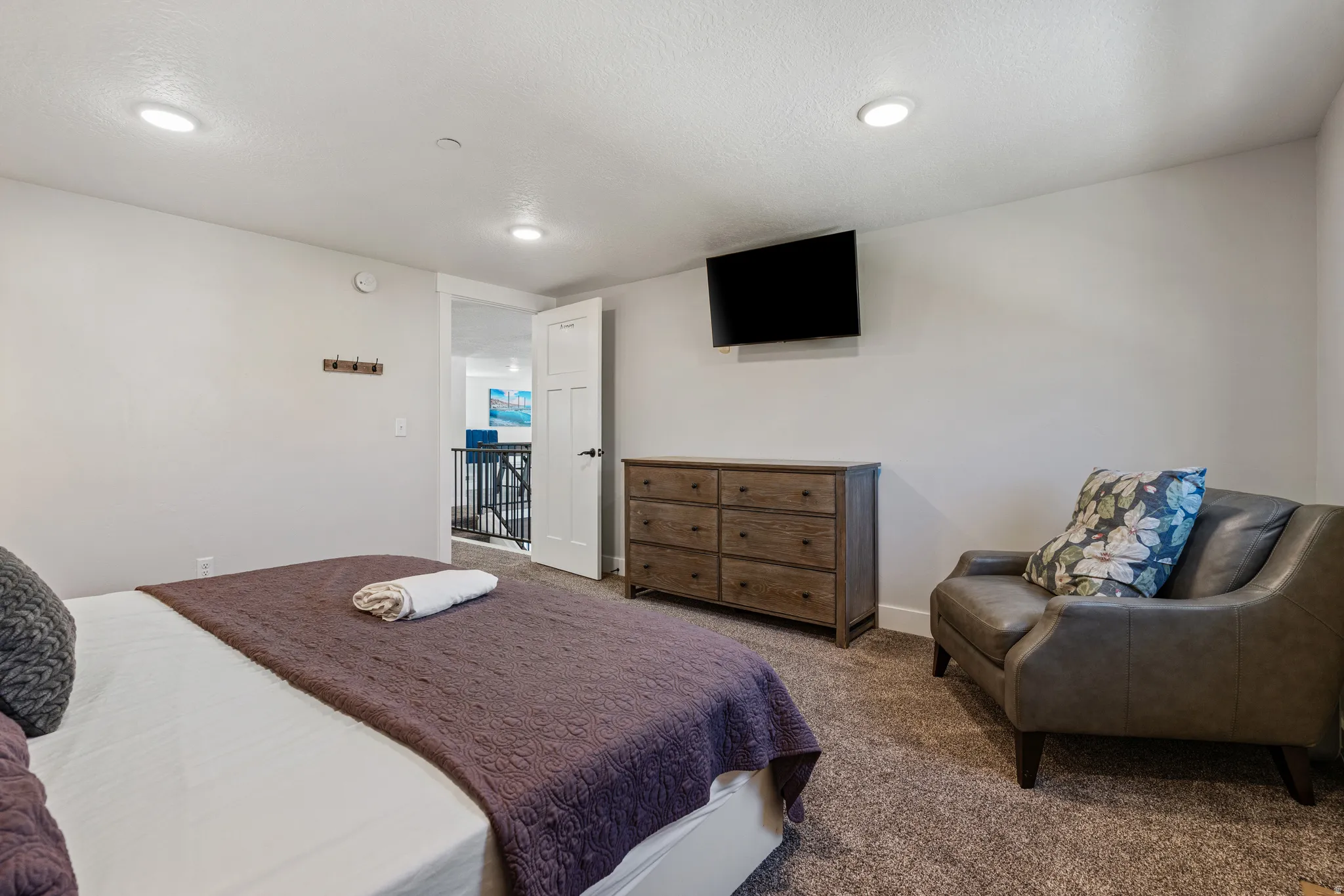 Recessed ceiling lighting, wall-mounted television, wood-finish dresser, and carpeted flooring