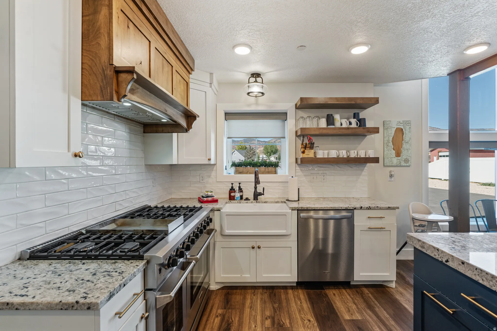 Gourmet kitchen featuring a professional-grade range, white subway tile backsplash, farmhouse sink, wood-finish flooring, and granite countertops