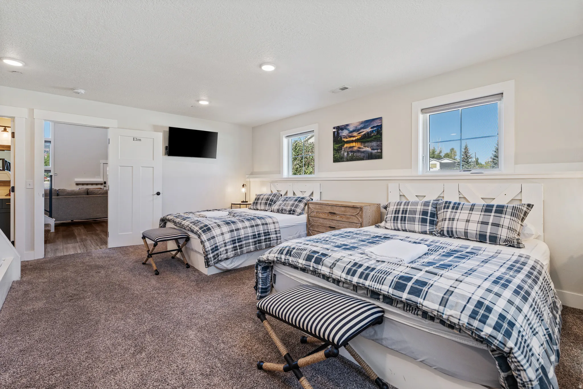 Recessed lighting, two windows with white trim, wood-finish headboards, and a wall-mounted flat-screen television