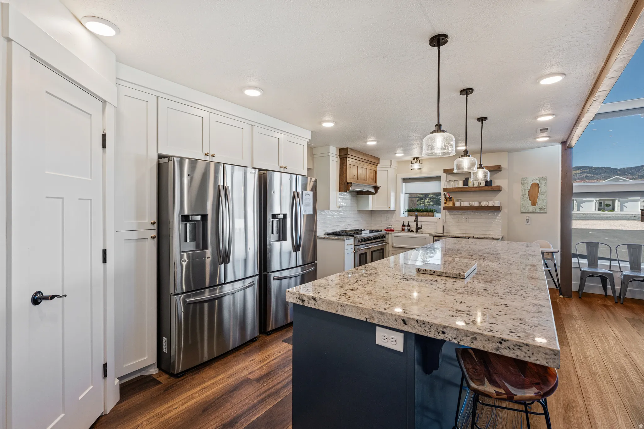 Gourmet kitchen with stainless steel appliances, extensive white cabinetry, a large center island with a stone countertop, and wood-finish flooring