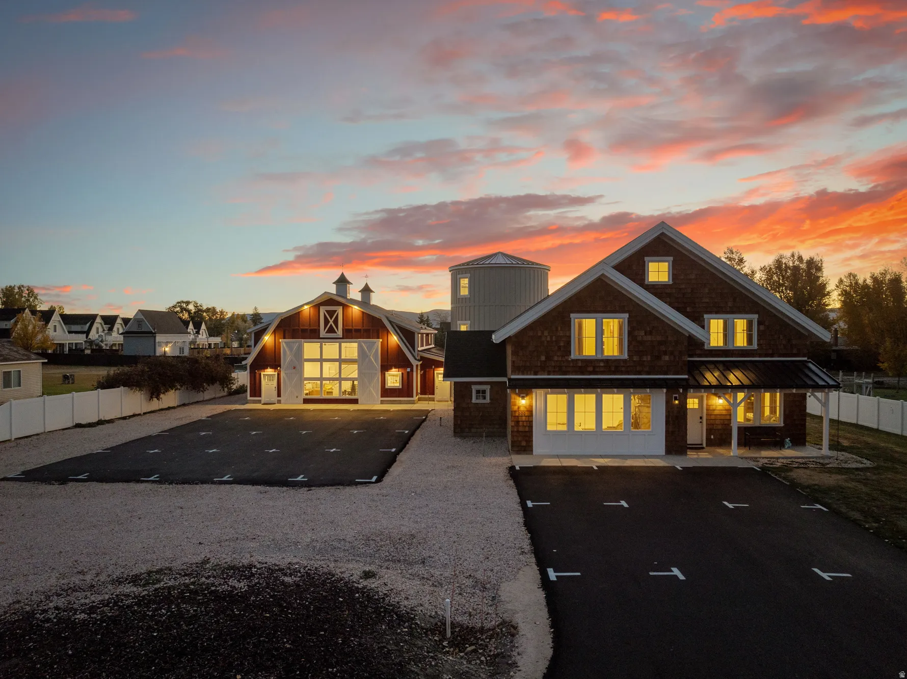 Barn-style auxiliary structure, shingle siding, white fencing, expansive gravel driveway, and paved parking area
