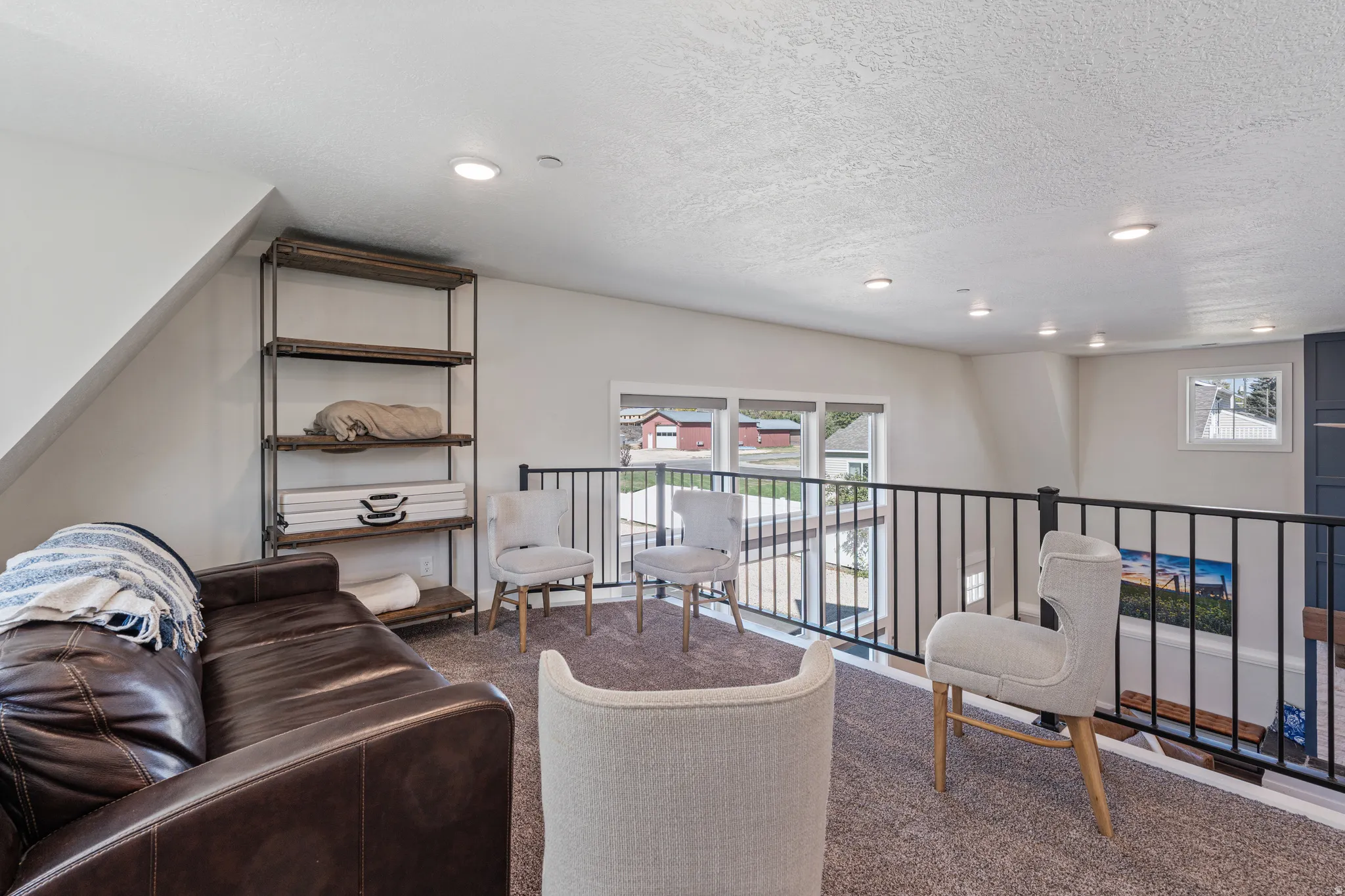 Loft area featuring carpeted flooring, recessed lighting, white walls, large windows, and a black metal railing