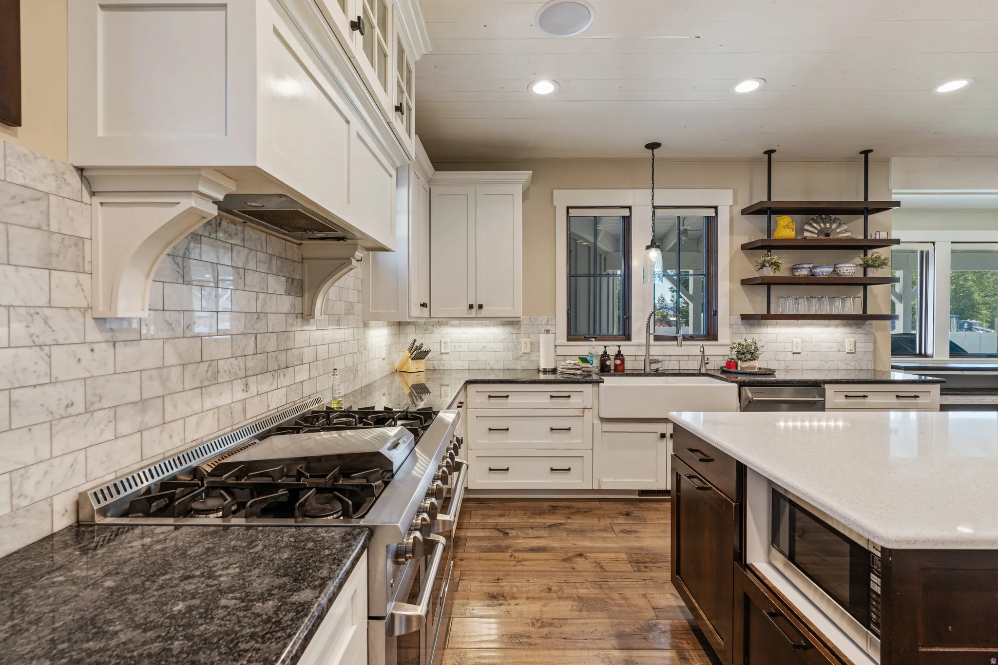 Gourmet kitchen featuring a professional-grade gas range, contrasting dark stone countertops, white subway tile backsplash, and a farmhouse sink