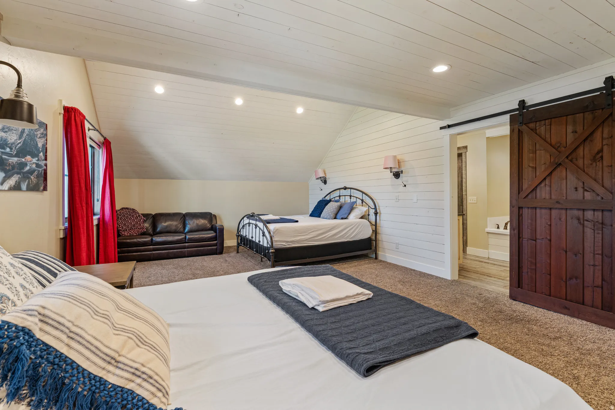 Vaulted ceiling with recessed lighting, shiplap wall paneling, dark wood-finish barn door, and wall-mounted sconces