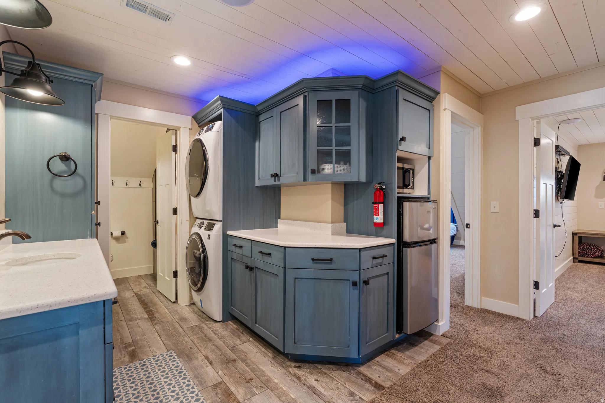Blue-painted cabinetry with white countertops, stacked laundry appliances, and wood-finish flooring