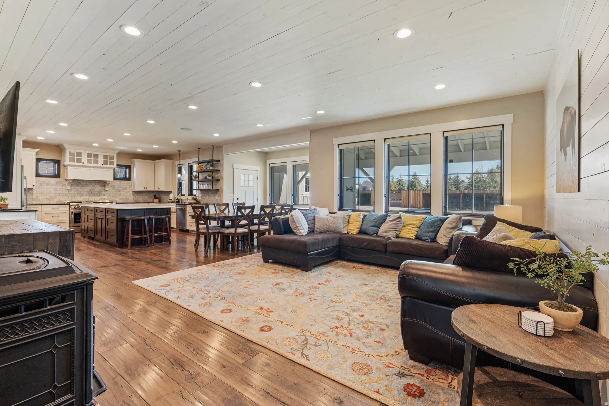 Open-concept living space with wood-finish flooring, recessed lighting, white shiplap ceiling, and a prominent kitchen island with seating