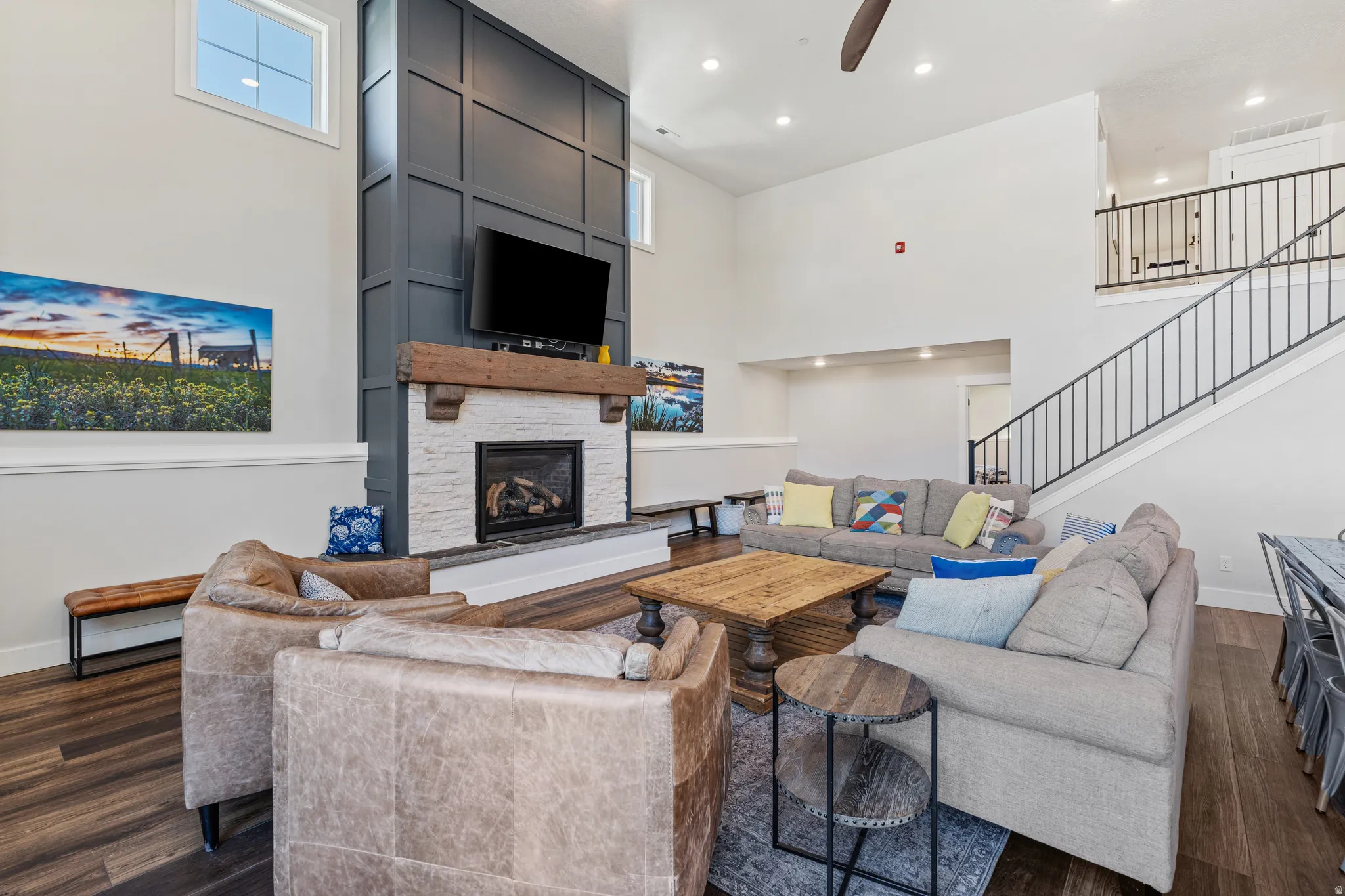 Two-story living area featuring a fireplace with a wood mantel, a paneled accent wall, a staircase with metal railings, and wood-finish flooring
