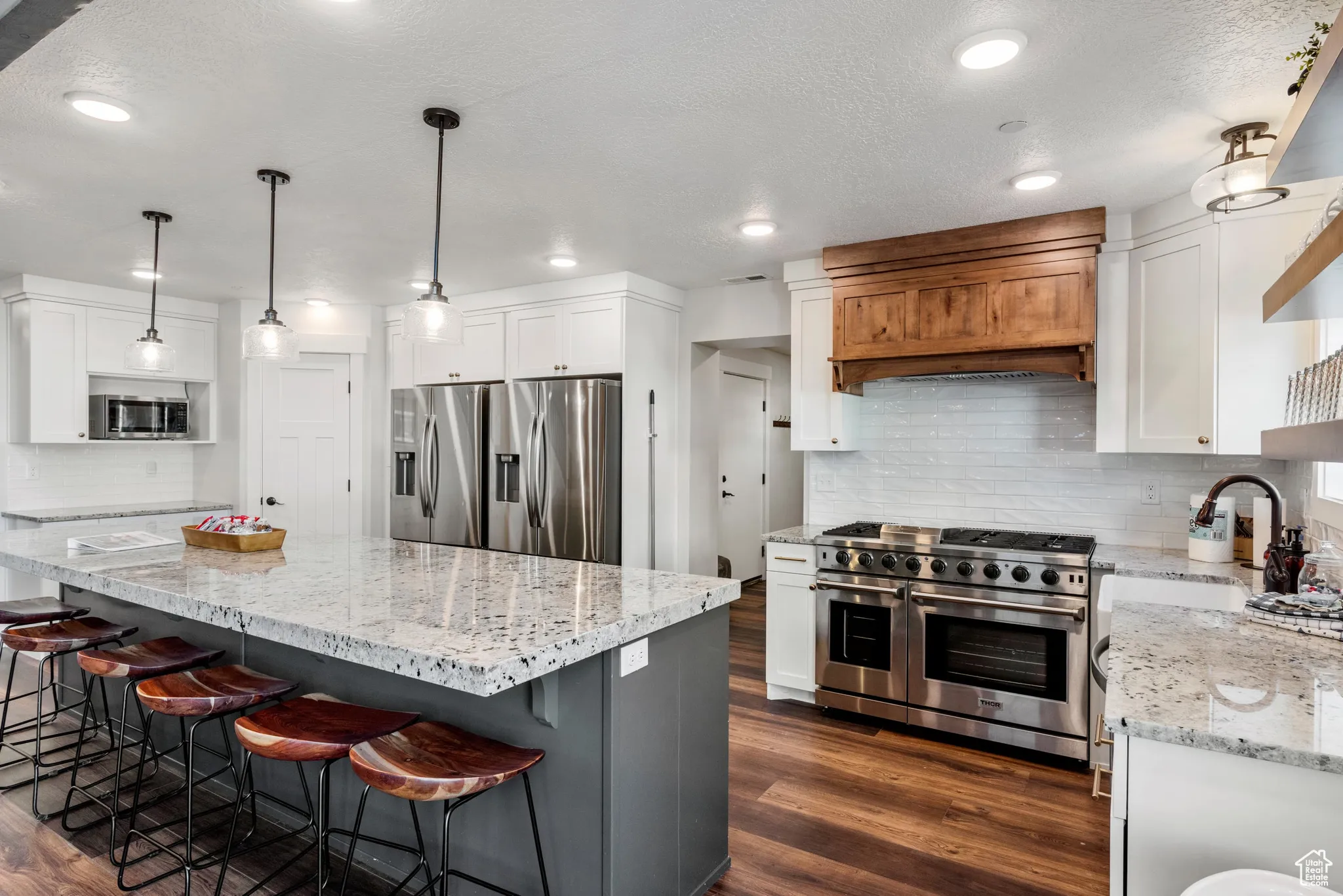 Kitchen with stainless steel appliances, white cabinets, decorative backsplash, light stone counters, and a textured ceiling