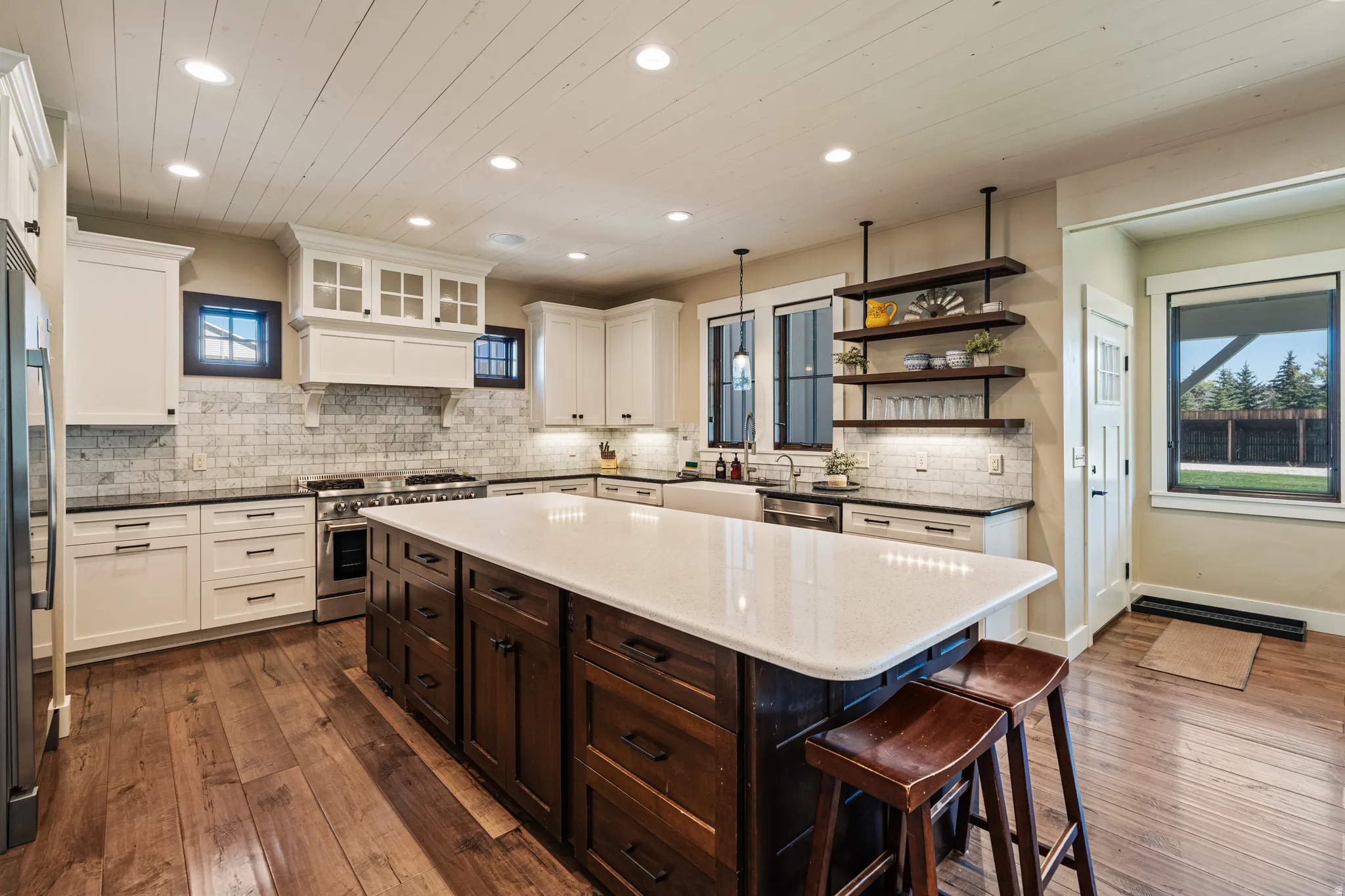Kitchen featuring wood-finish flooring, white cabinetry, a large center island with a light-toned countertop, and a tile backsplash