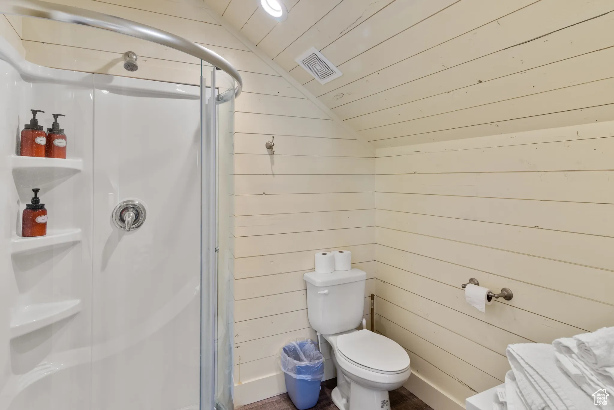 Bathroom with vaulted ceiling, wooden walls, a shower stall, wooden ceiling, and toilet