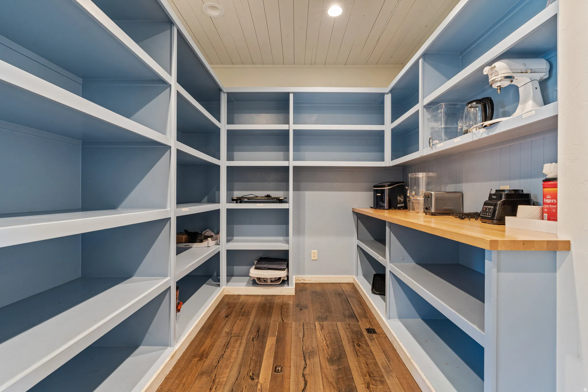 Spacious pantry featuring extensive built-in shelving, a wood-finish countertop, wood-finish flooring, and a beadboard ceiling