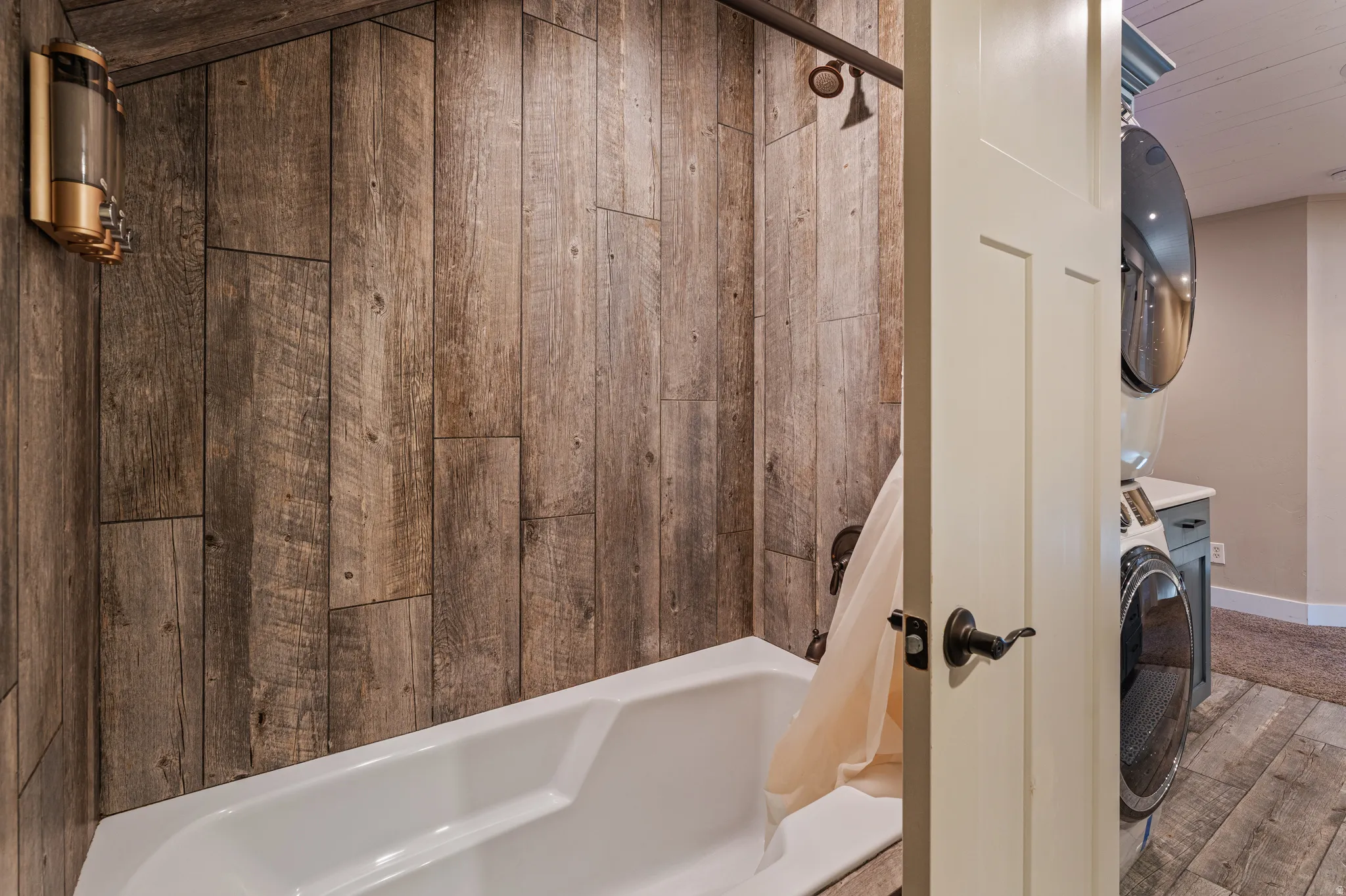 Wood-finish wall paneling, white bathtub, and brushed bronze shower fixtures