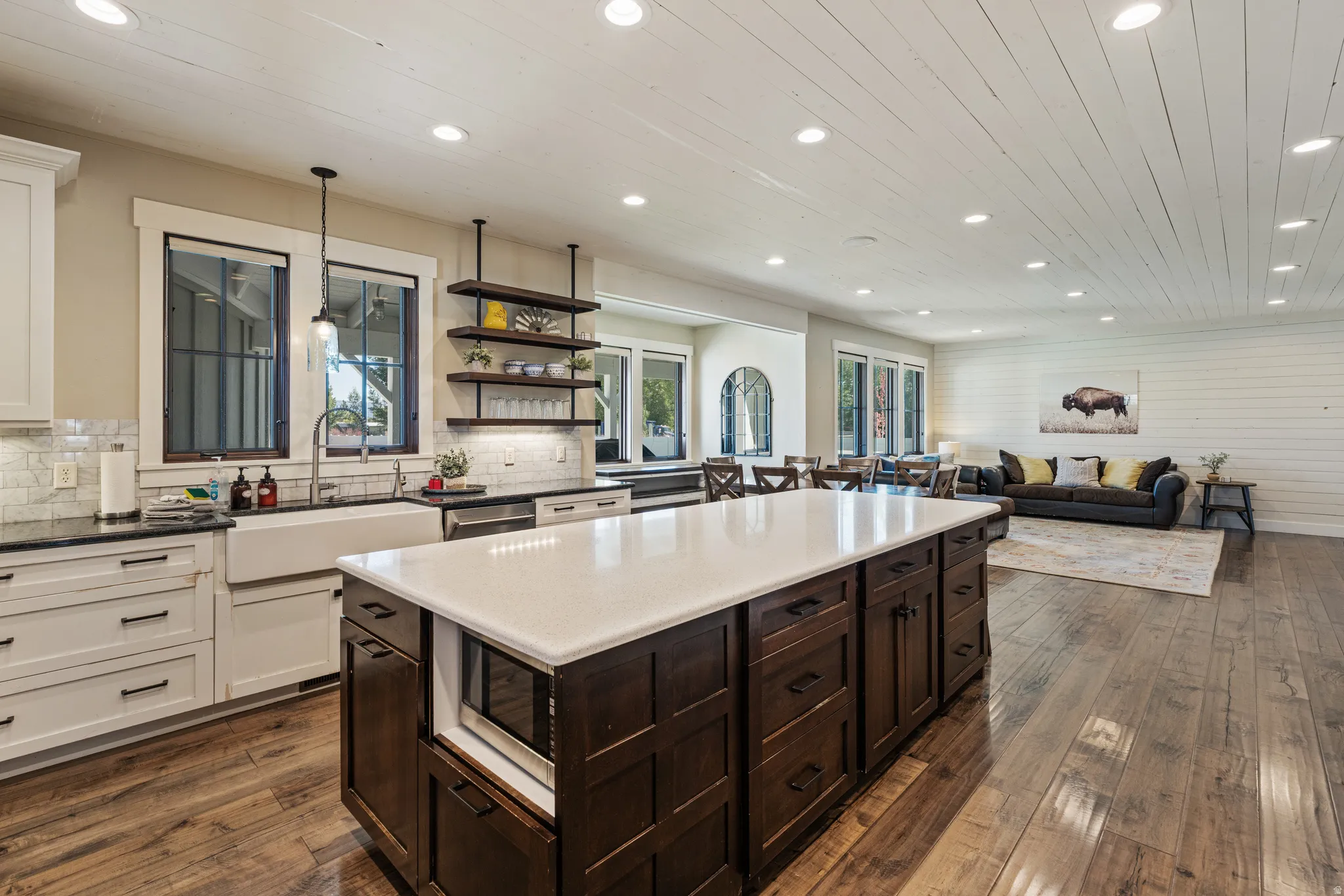 Spacious kitchen featuring an expansive central island with a light-toned countertop, wood-finish flooring, and white upper and lower cabinetry with dark hardware