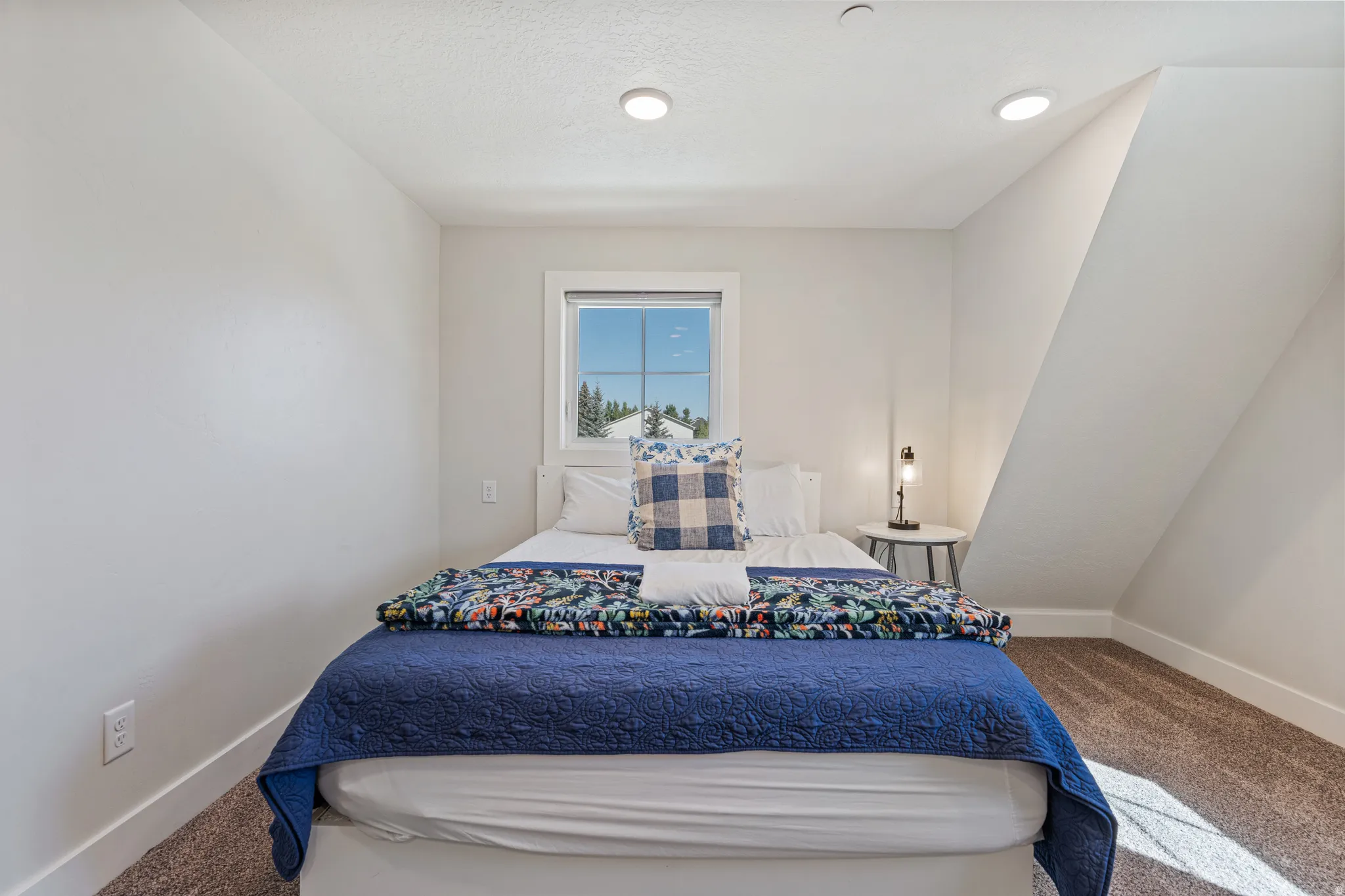 White painted walls, recessed ceiling lighting, a single window, and sloped ceiling details