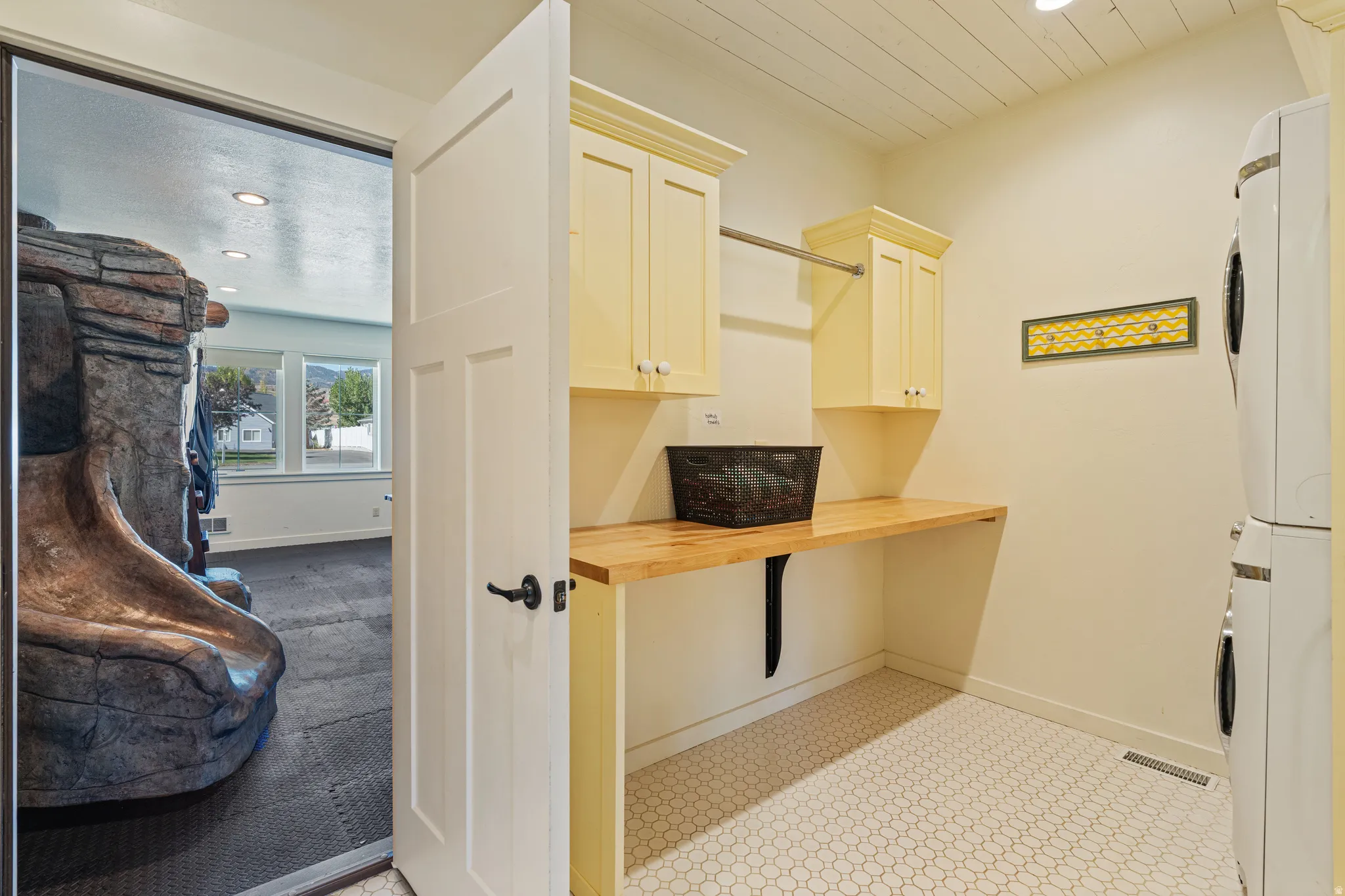 Laundry area featuring white honeycomb tile flooring, light-colored upper cabinetry, and wood-finish countertops