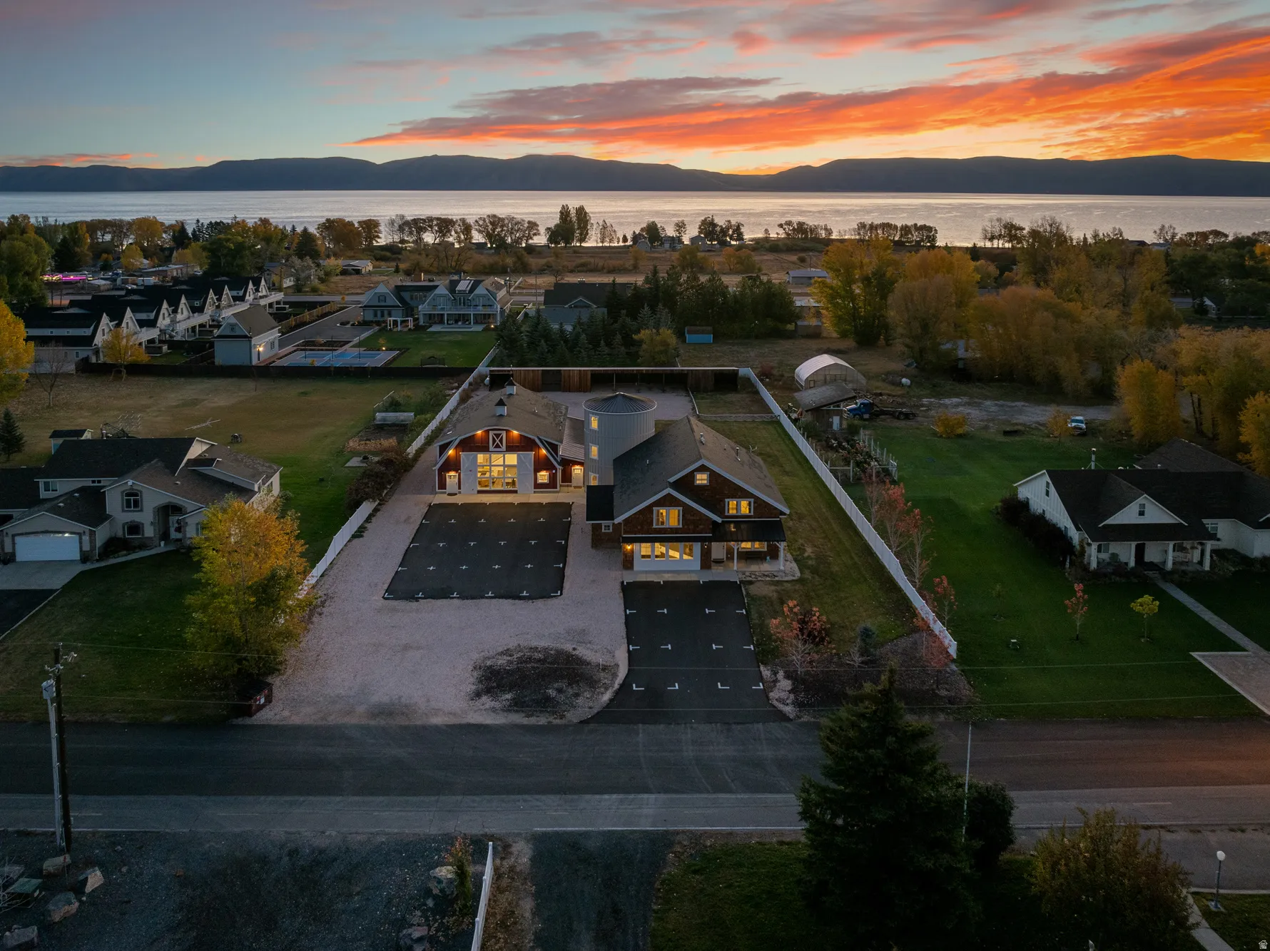 Expansive property featuring two distinct structures, a substantial driveway, mature trees, and a white perimeter fence