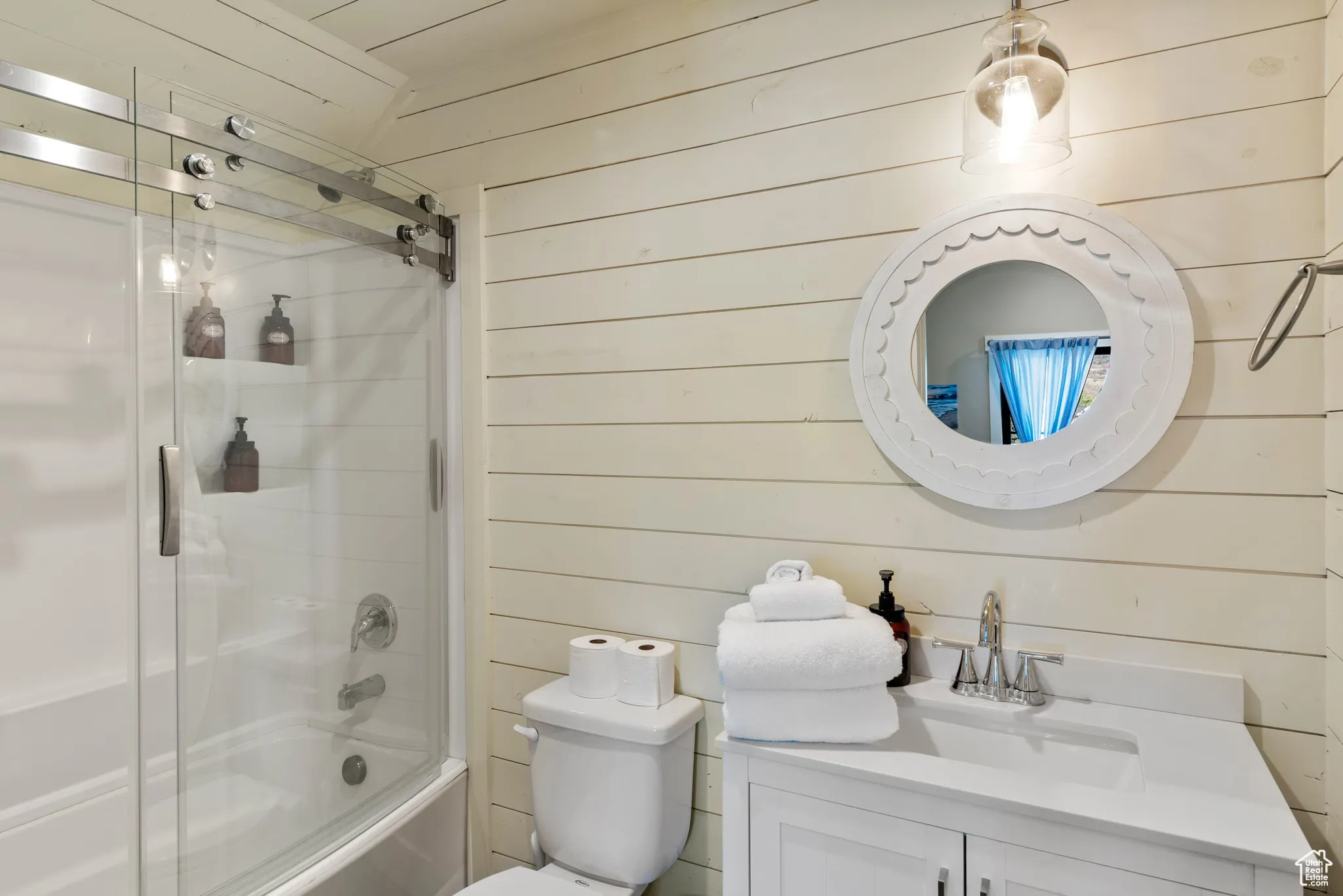Bathroom with wood walls, vanity, shower / bath combination with glass door, and toilet