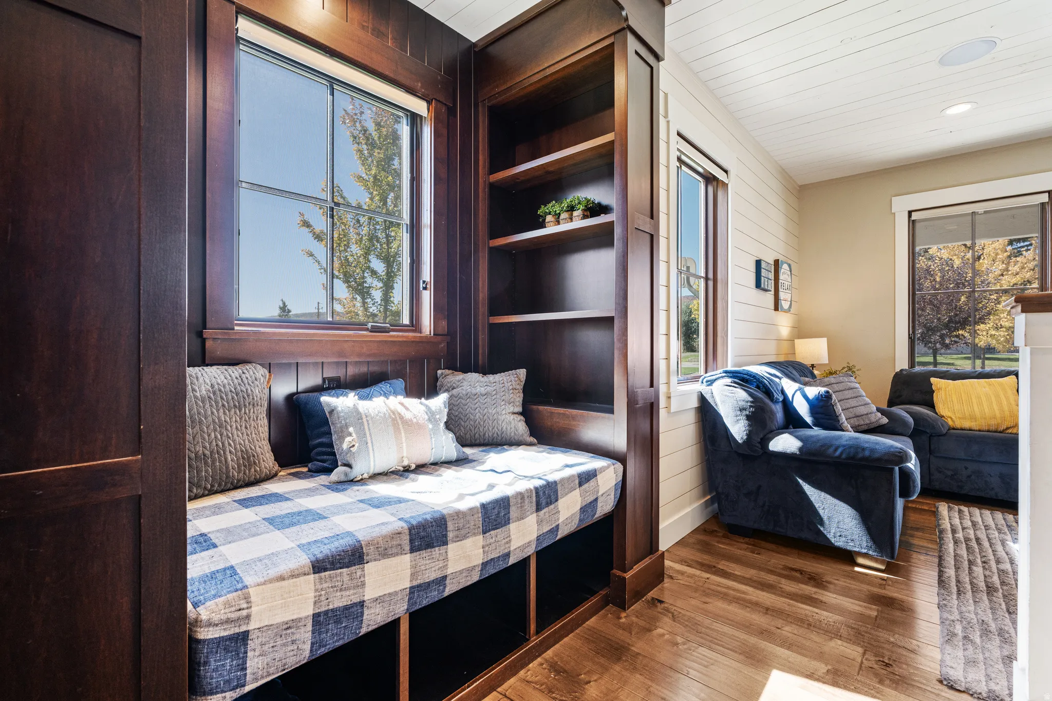 Built-in window seat with integrated shelving, wood-finish flooring, and white shiplap accent wall