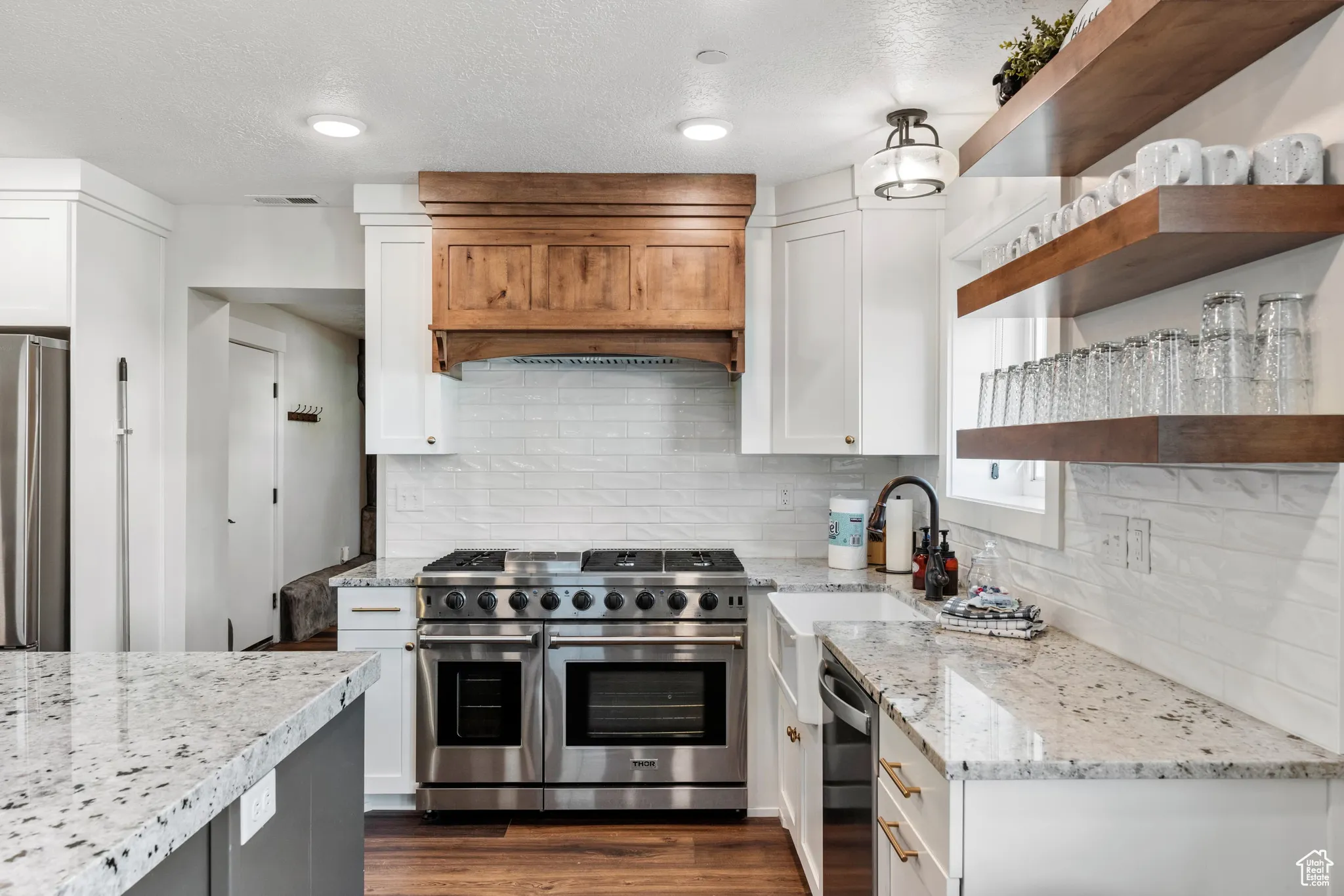 Kitchen featuring stainless steel appliances, open shelves, white cabinets, light stone countertops, and tasteful backsplash