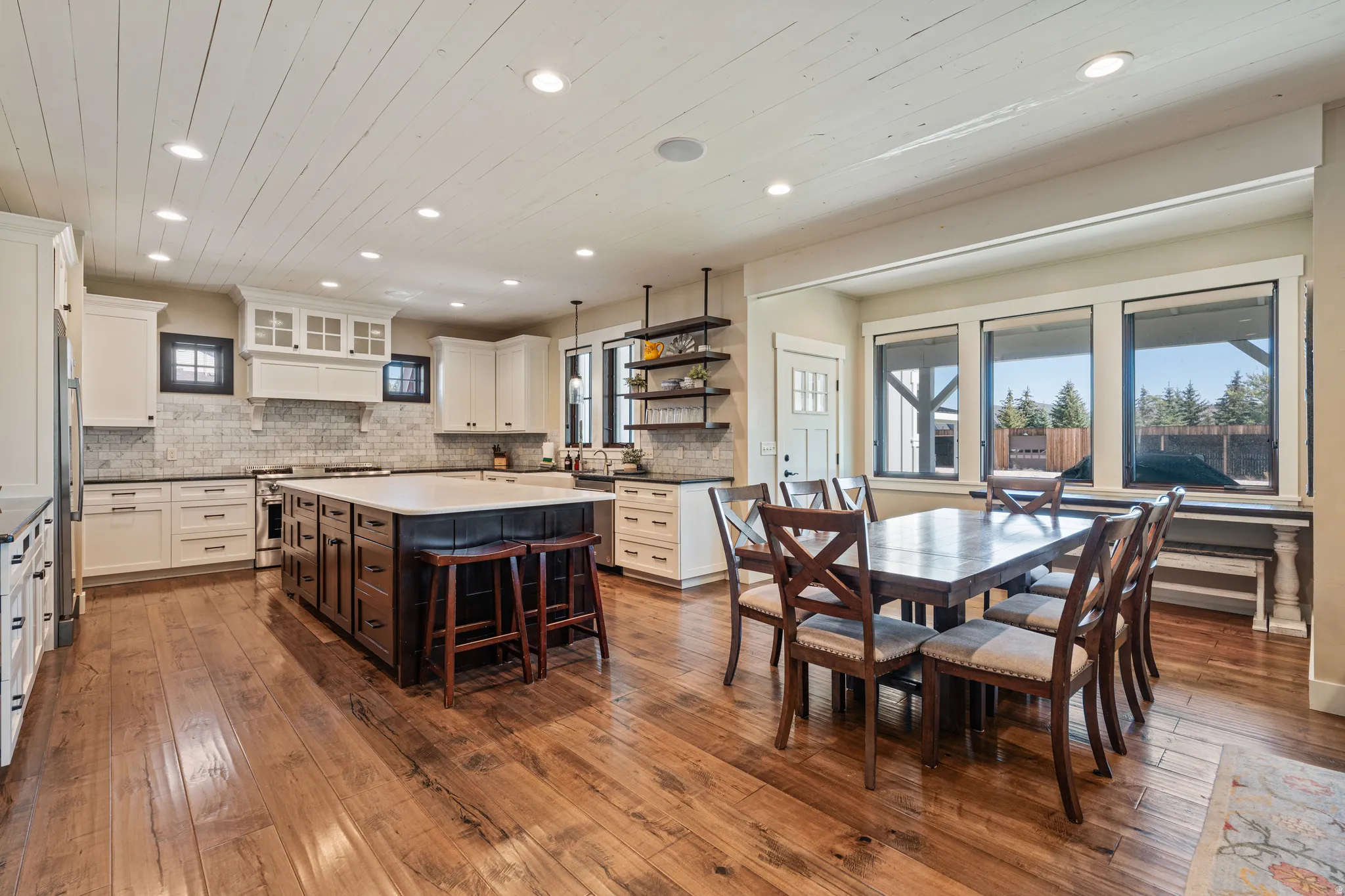 Spacious kitchen and dining area featuring wide-plank wood flooring, a large kitchen island with seating, recessed lighting, and ample natural light through multiple windows