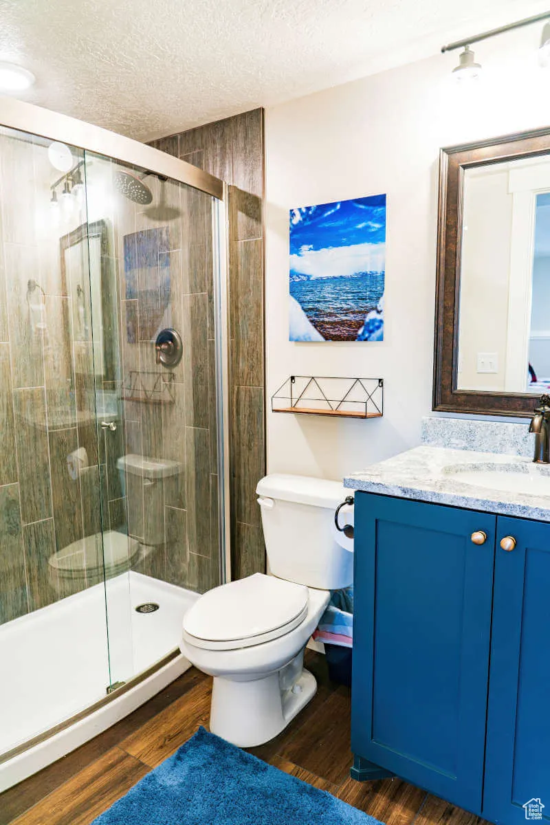 Full bathroom with vanity, toilet, a textured ceiling, a stall shower, and wood finished floors