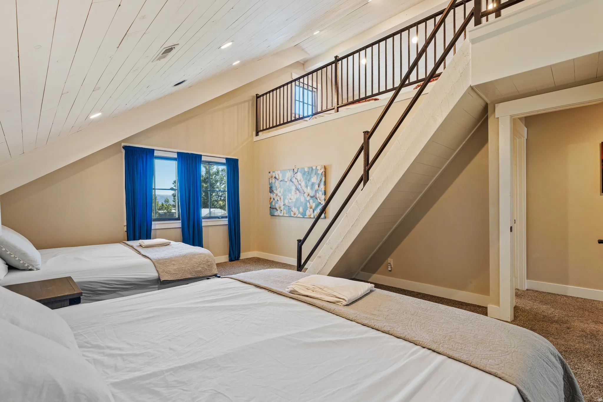 Vaulted plank ceiling, integrated lighting, lofted area with metal railing, multiple windows, and carpet flooring