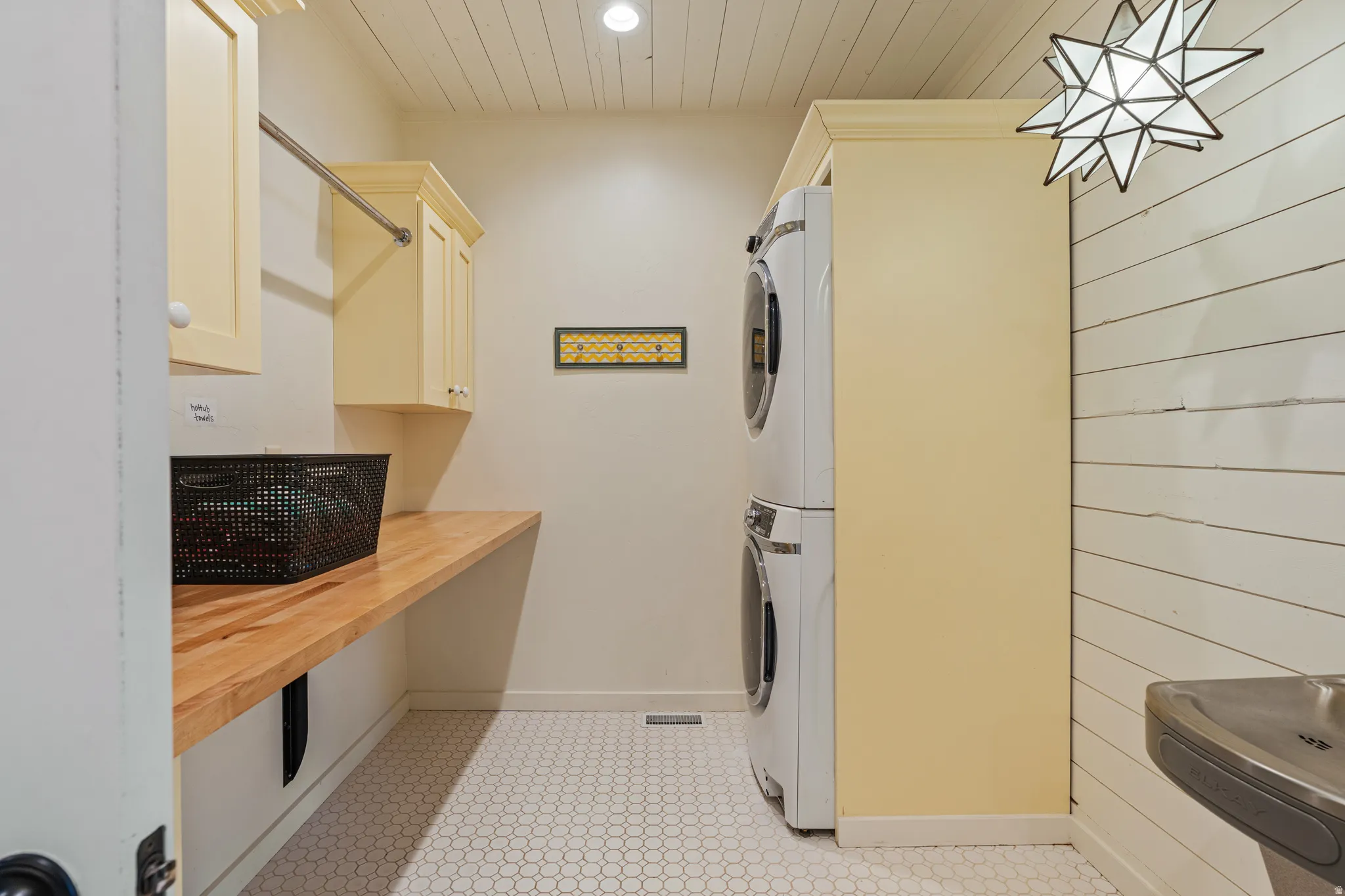 Stacked washer and dryer, wood-finish countertop, upper cabinetry, hexagon tile flooring, and shiplap wall detail