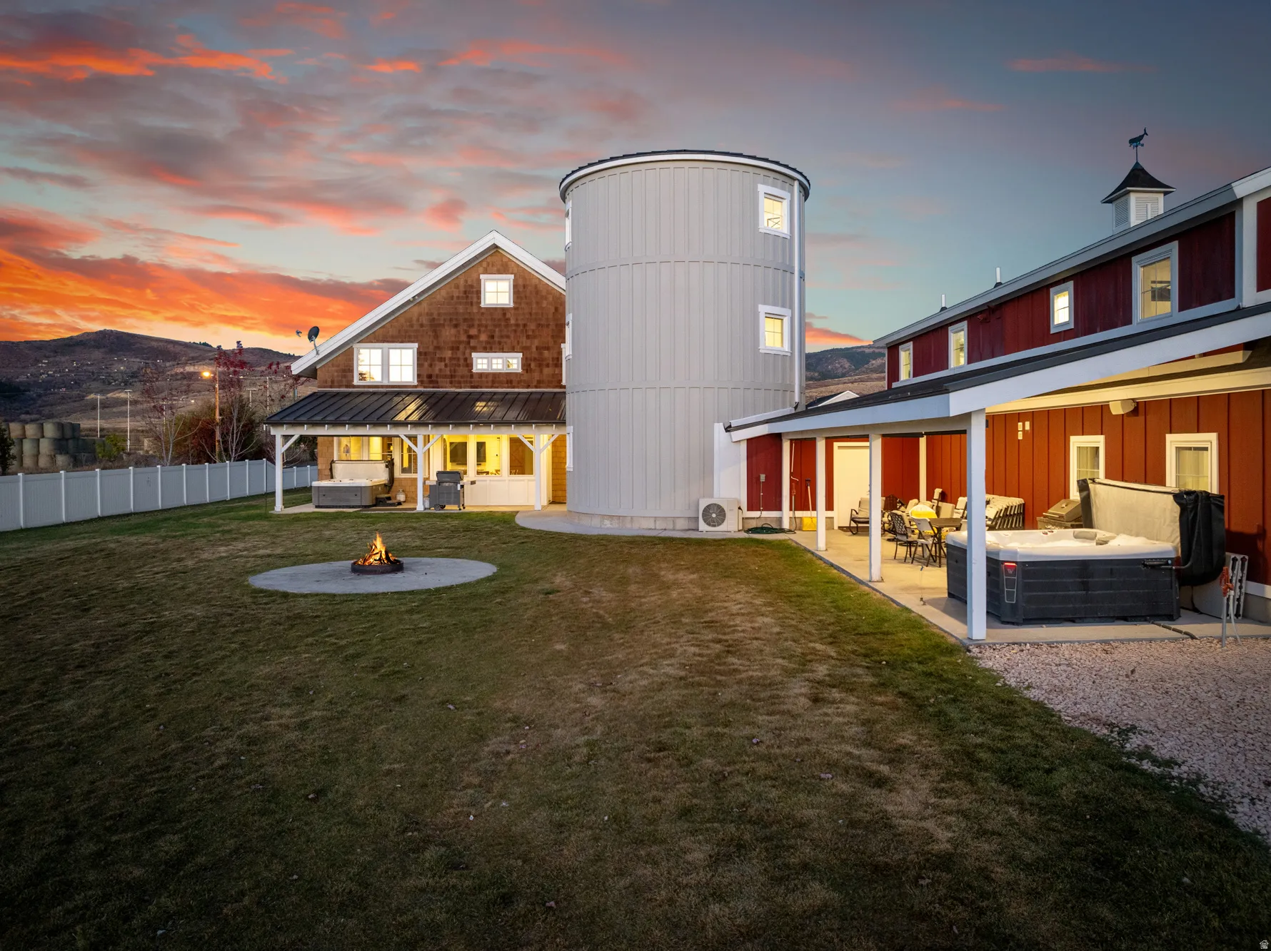 Spacious backyard featuring a manicured lawn, dedicated fire pit area, covered patio, and attached hot tub