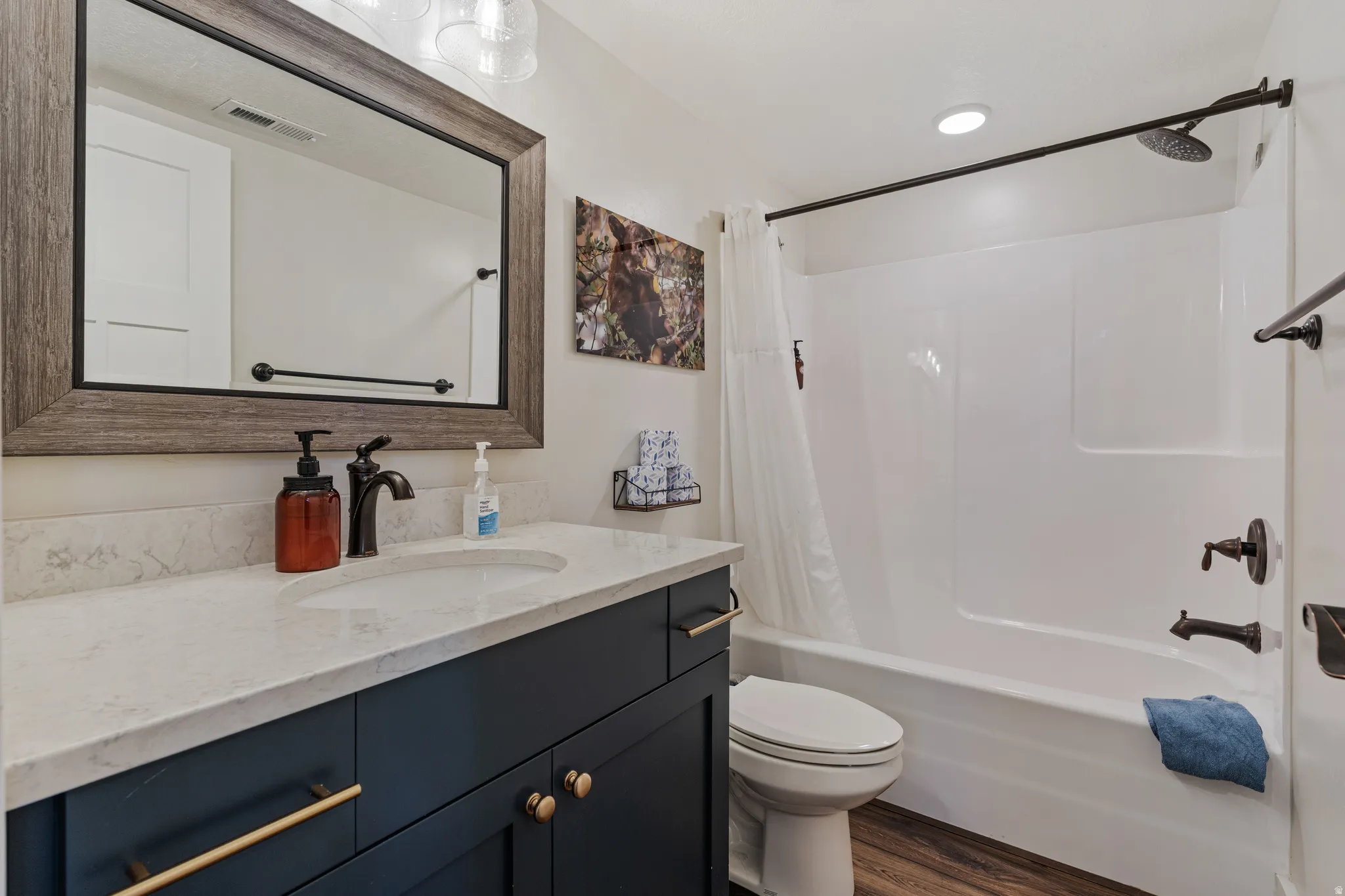 Bathroom featuring a dark wood-finish vanity with gold-tone hardware, white countertop with integrated sink, wood-framed mirror, and a shower/tub combination with dark-tone fixtures