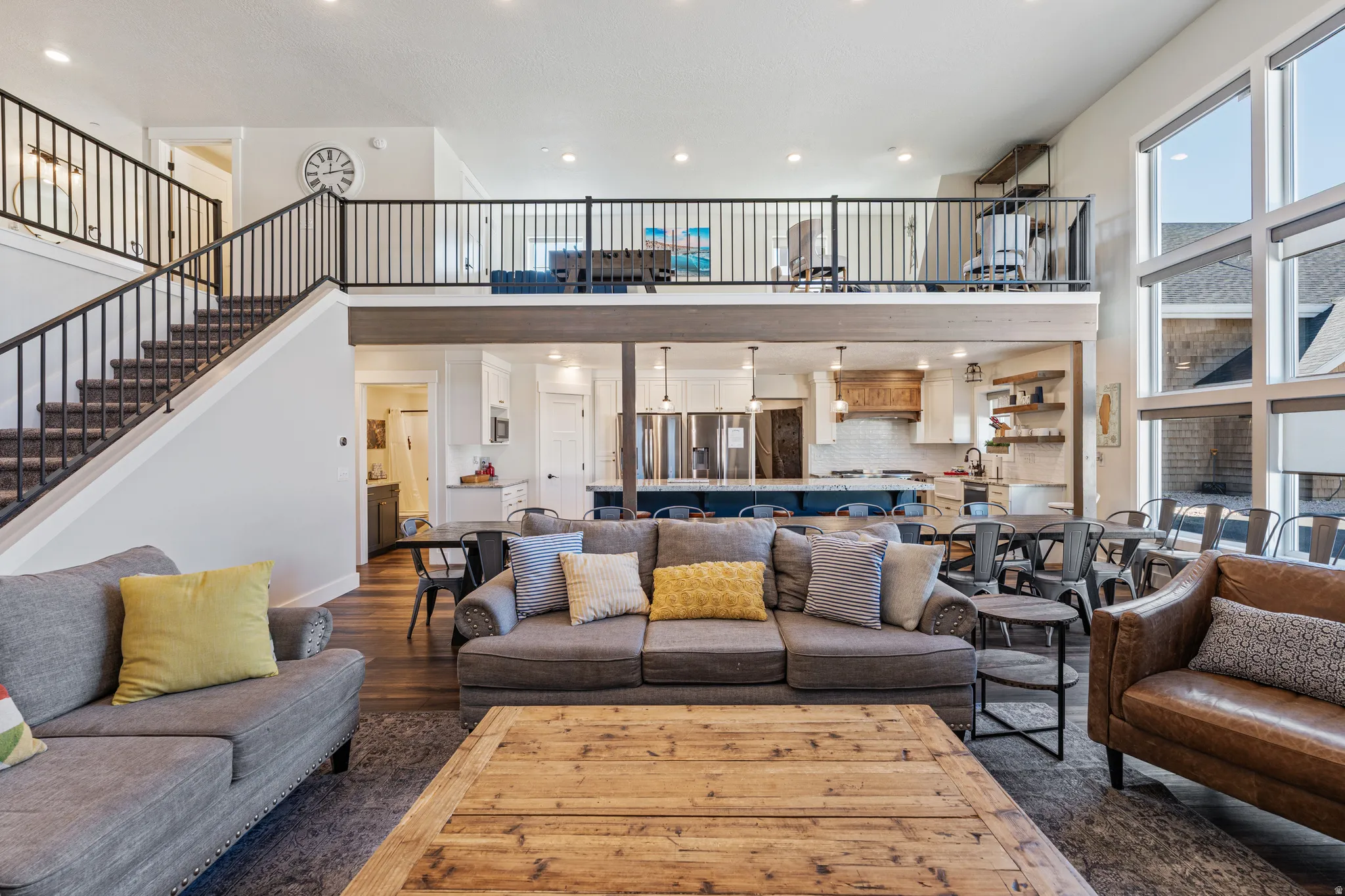 Two-story living area with high ceilings, large windows, an open kitchen with a central island, and a second-level balcony