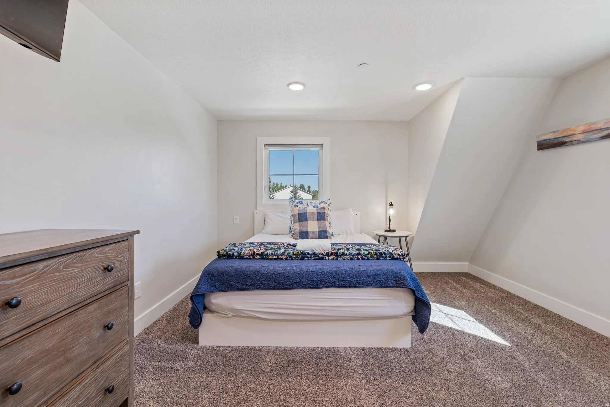 Recessed lighting, window with grid pattern, sloped ceiling, textured carpet, and neutral wall paint