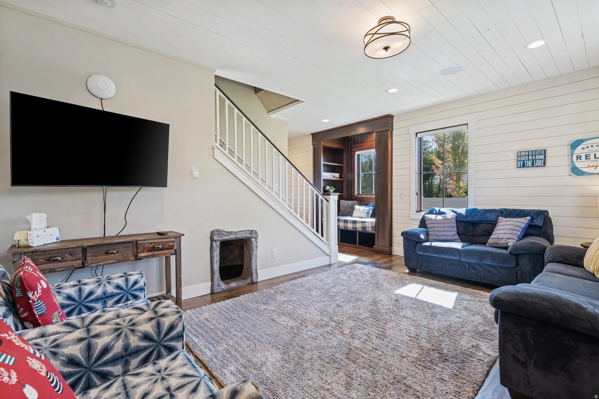 White shiplap accent wall, built-in window seat with storage, wood-finish flooring, staircase with white railings, and a decorative ceiling light fixture