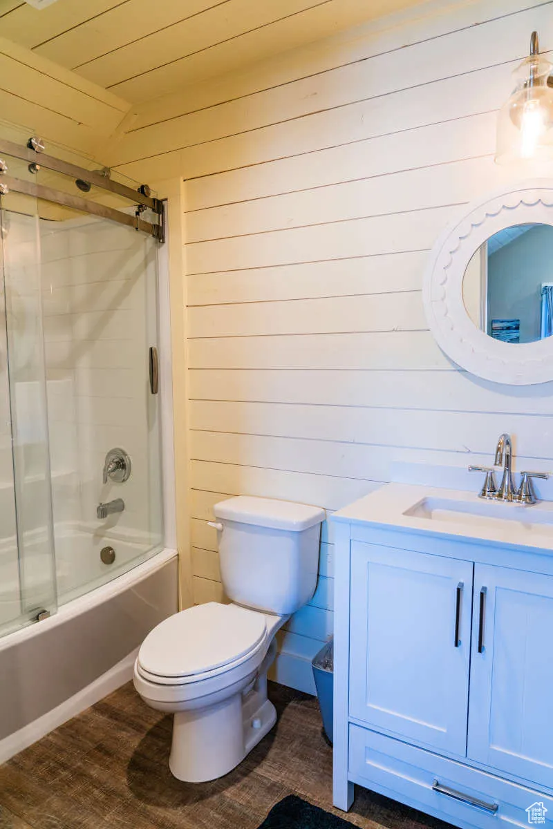 Full bathroom featuring wooden walls, toilet, vanity, shower / bath combination with glass door, and wood finished floors