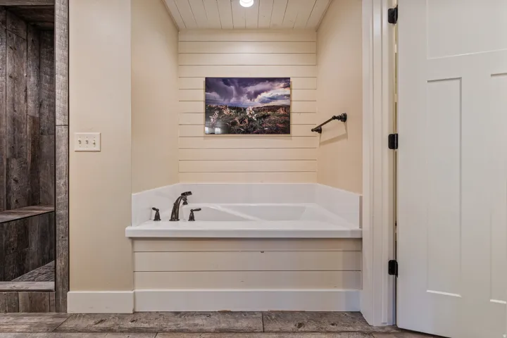 Built-in bathtub with dark bronze fixtures, shiplap wall accents, wood-finish flooring, and a barn wood-style shower enclosure