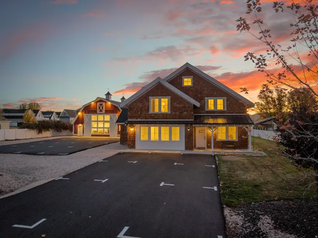 Shingle-sided home featuring a covered front porch with exposed beams, an asphalt driveway, and a gravel parking area
